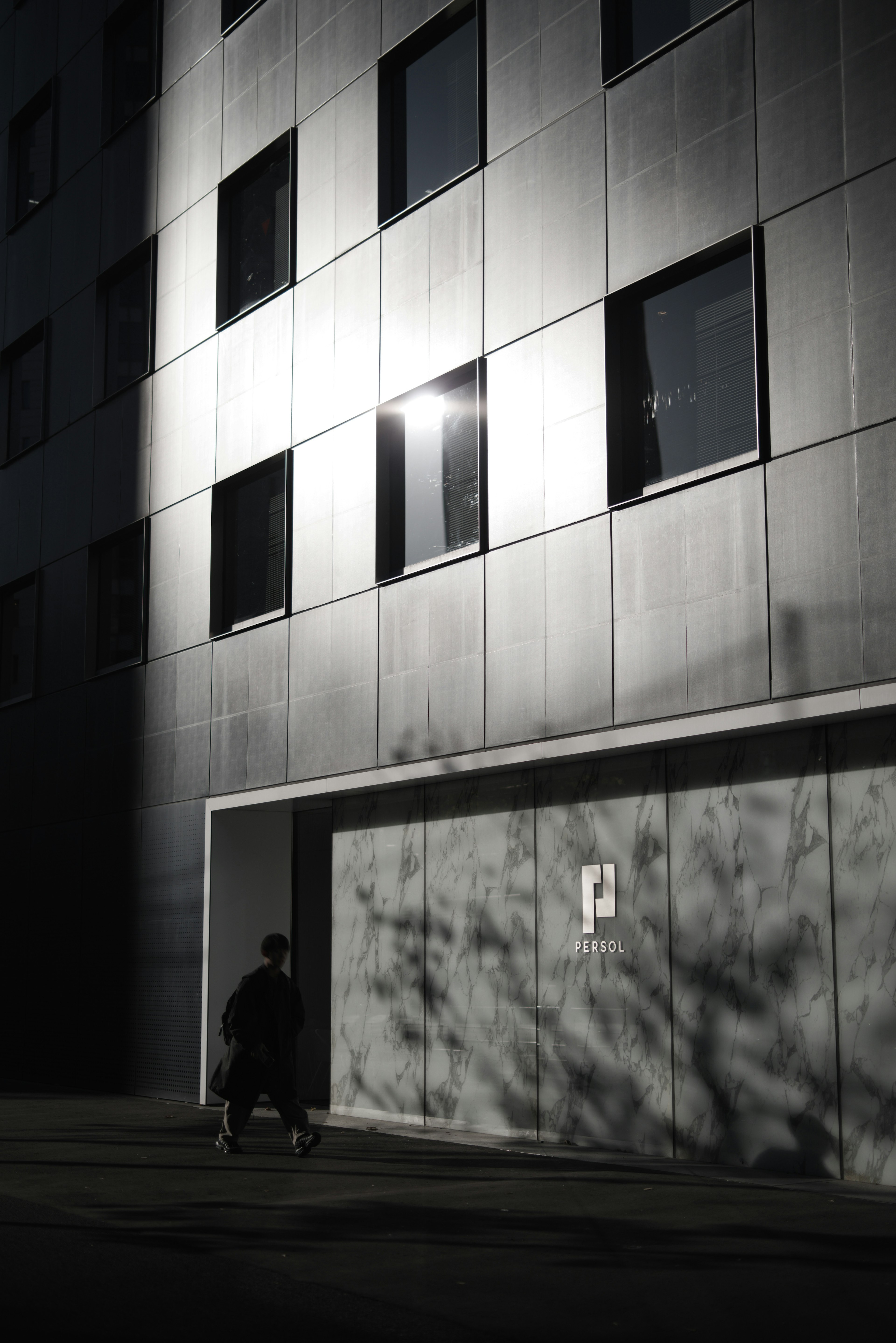 Image featuring a modern building facade with reflections and a shadowed figure