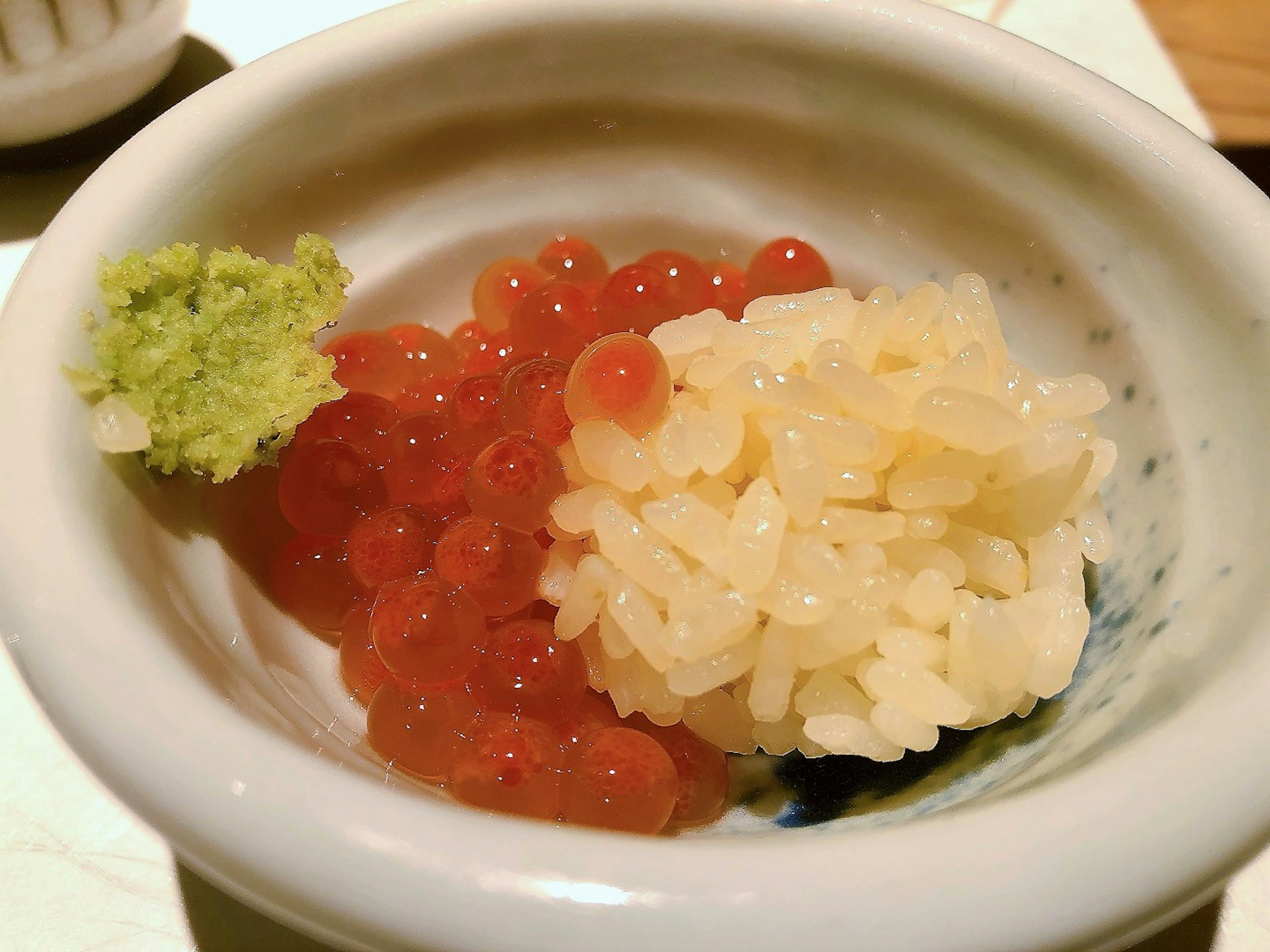 Un plato pequeño con arroz blanco e ikura roja adornado con wasabi