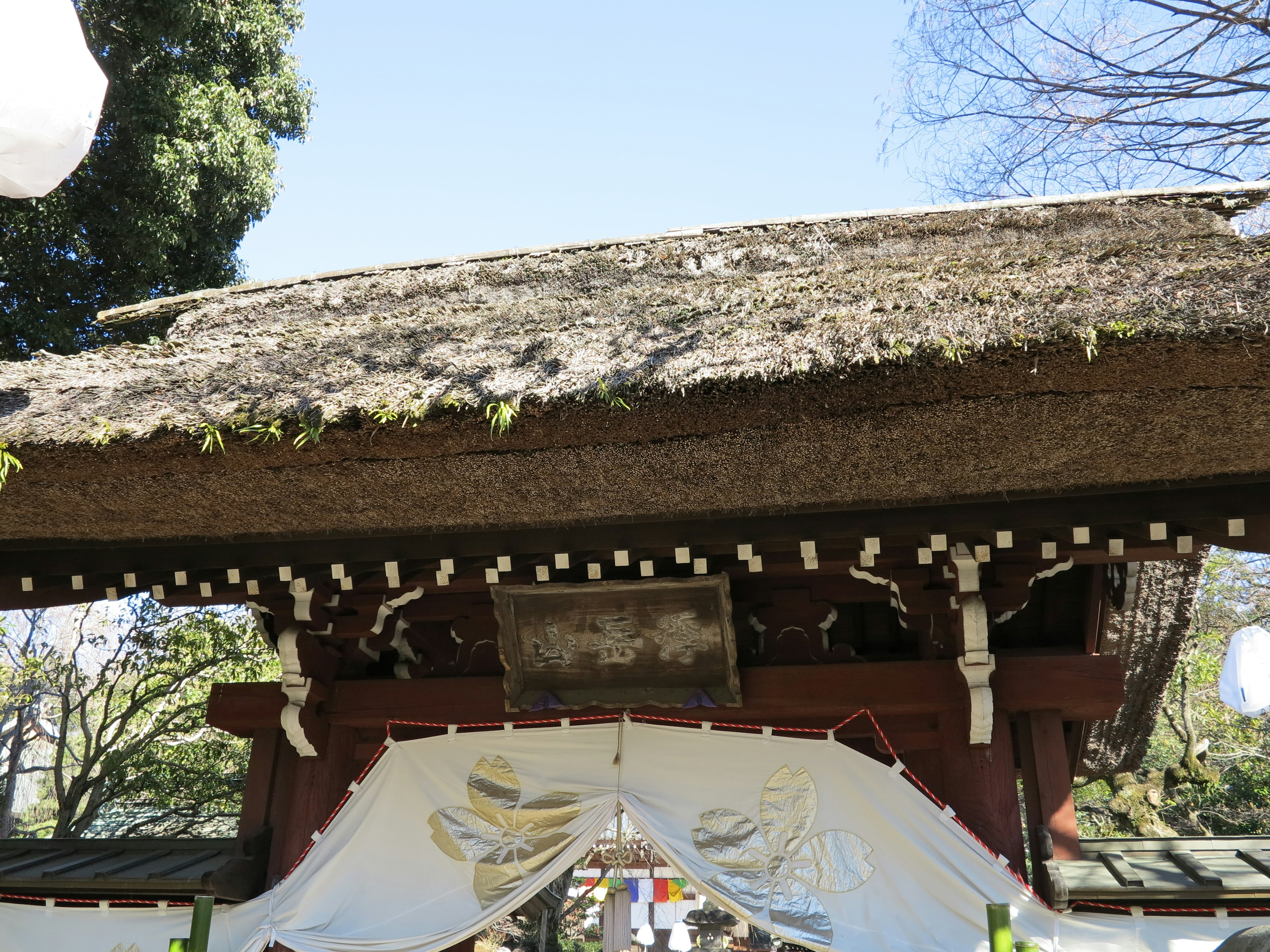 Porte de sanctuaire japonais traditionnel avec toit de chaume sculptures en bois décoratives et rideau en tissu blanc