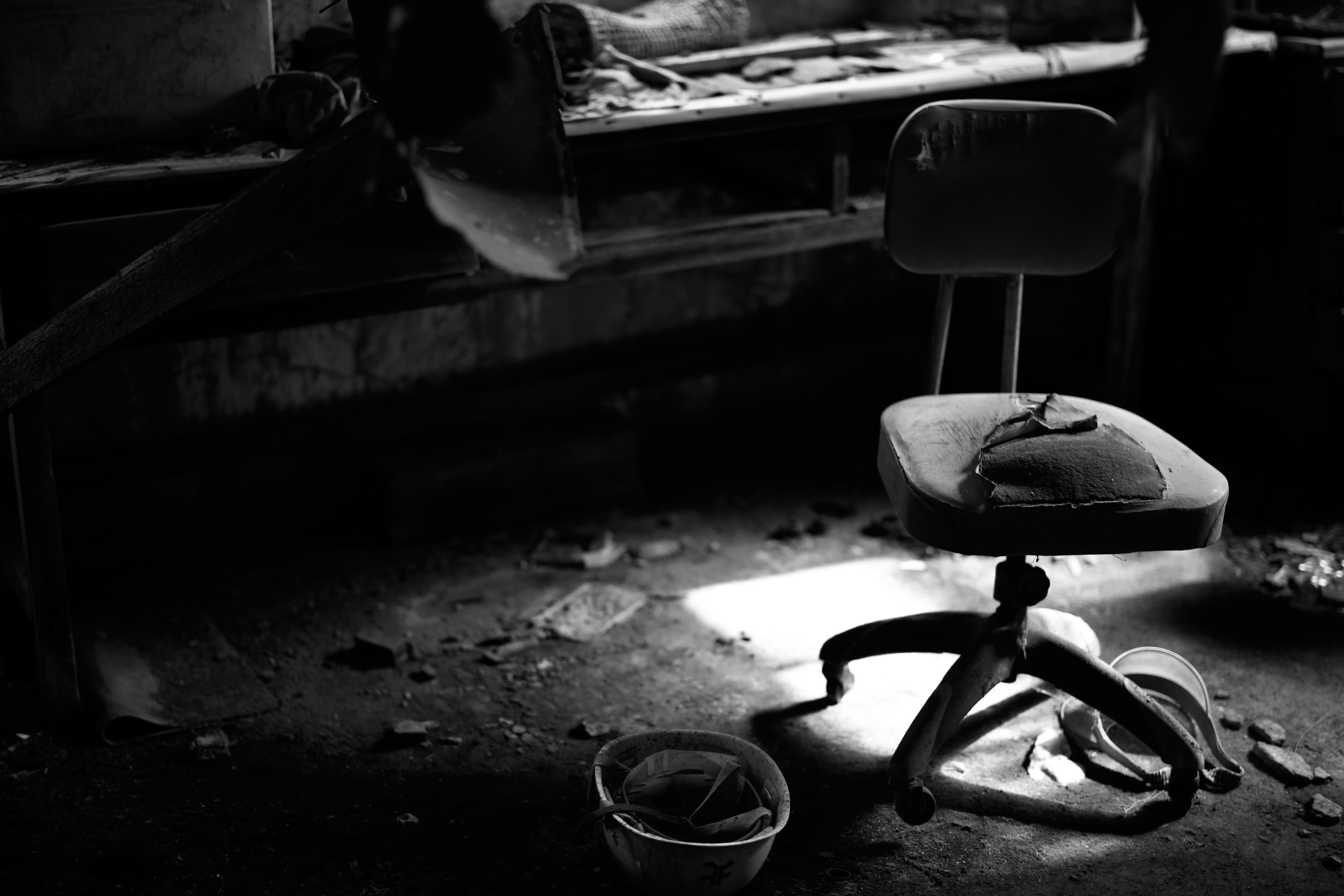 Old swivel chair in a dark room with light shining on the floor and cluttered desk