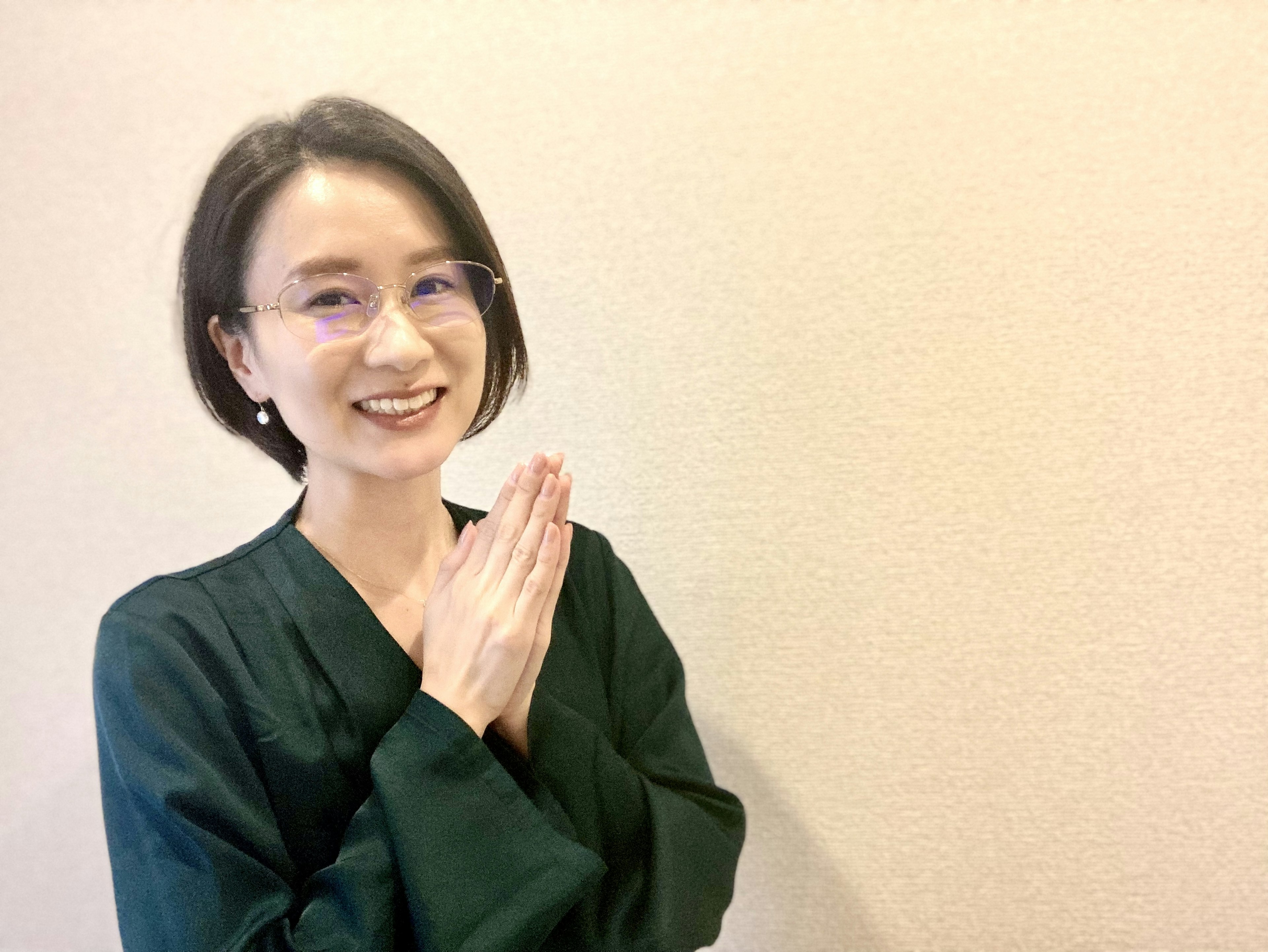 Femme en tenue verte souriant avec les mains jointes