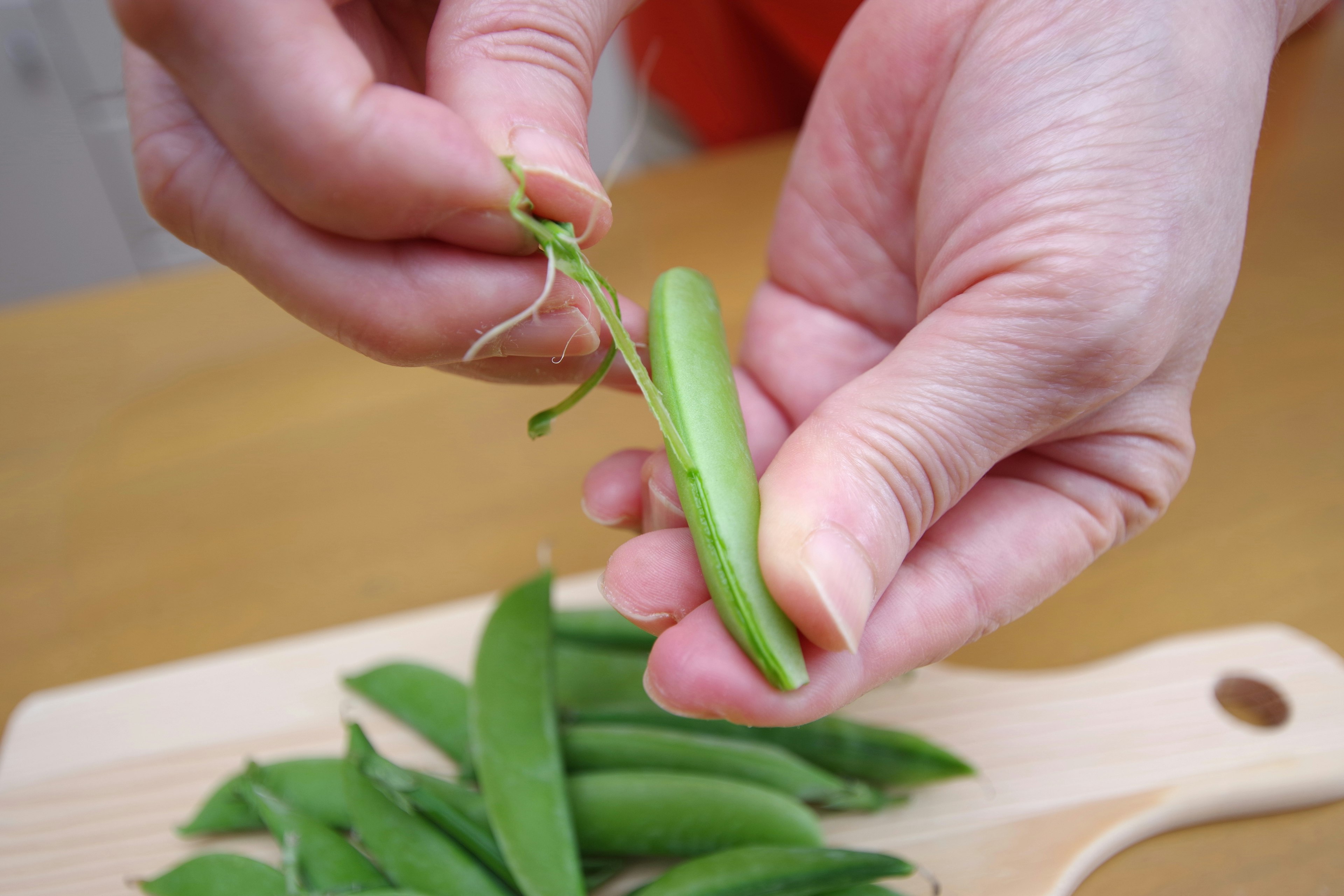 手にエンドウ豆を持ち、豆を取り出している様子