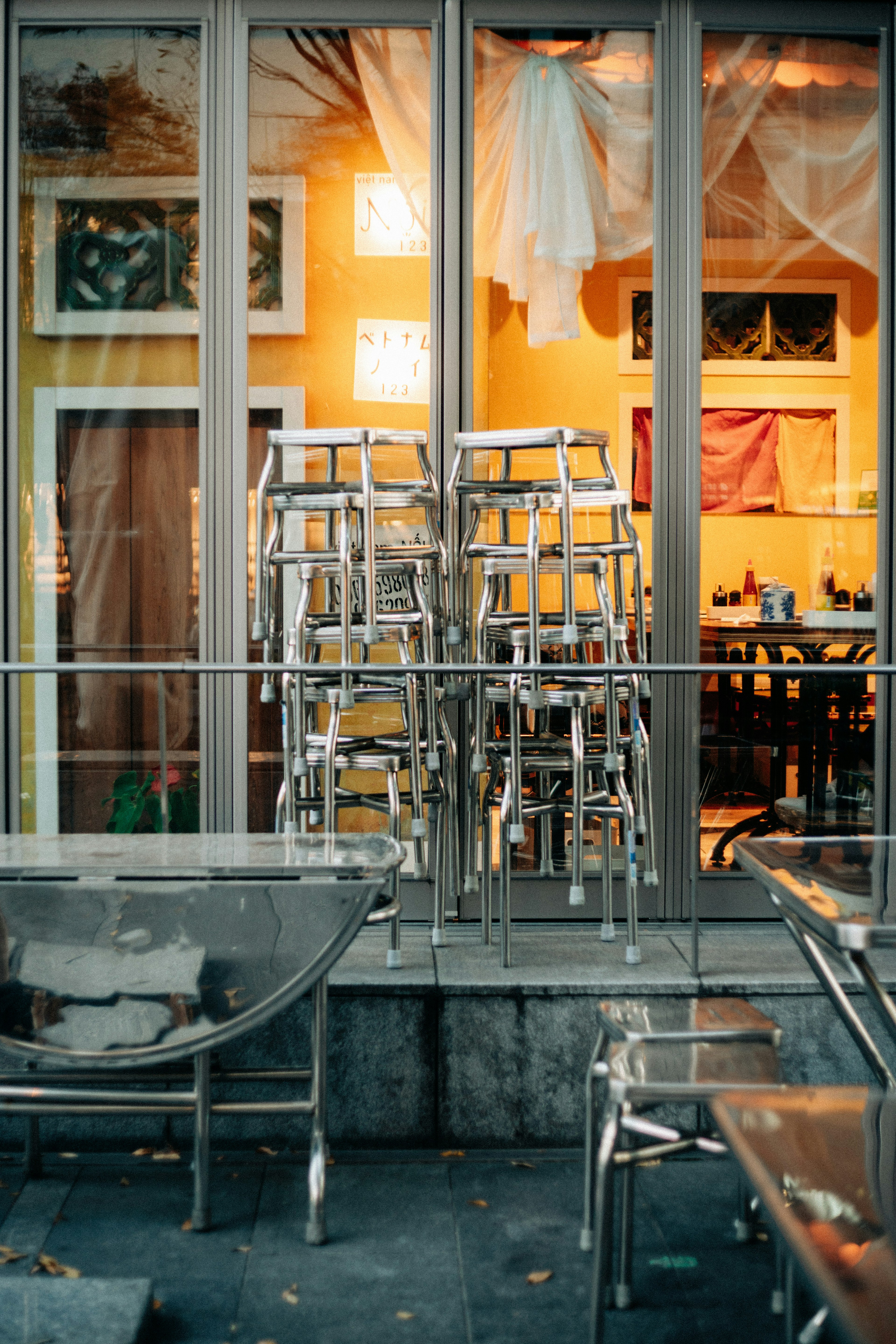 View through a café window showcasing stacked chairs and a yellow interior