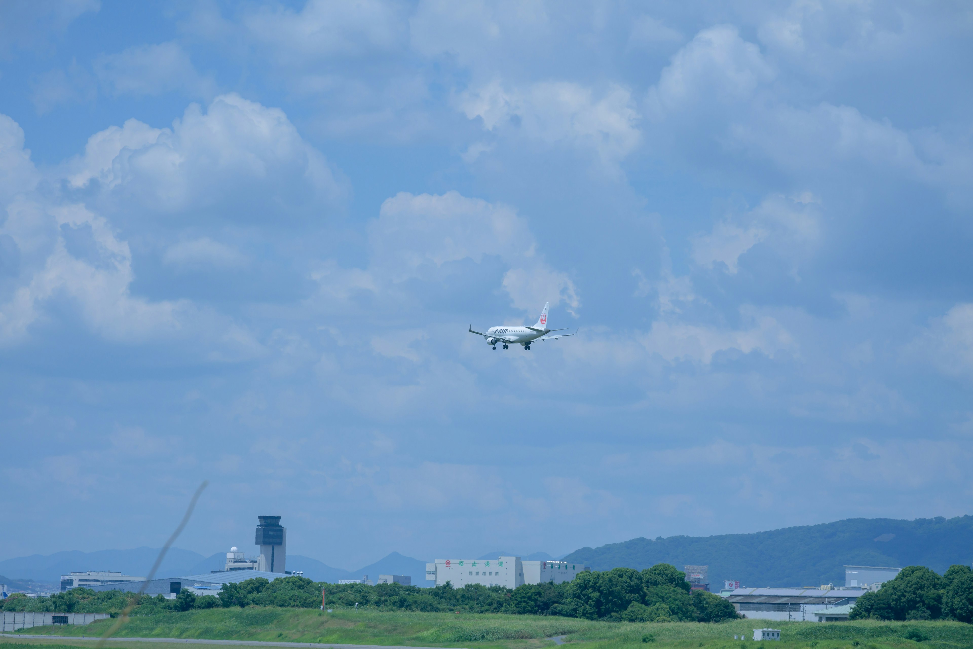 A white aircraft flying under a blue sky with fluffy clouds and green landscape