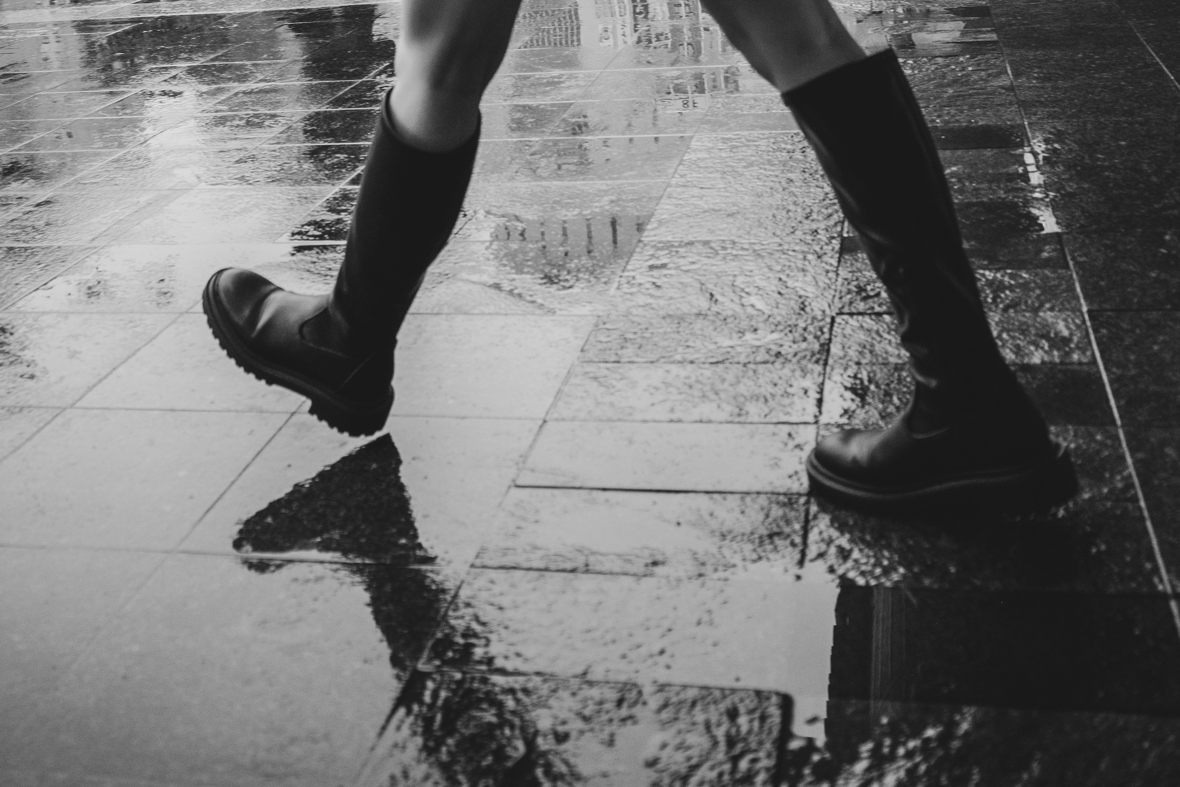 Pieds dans des bottes de pluie noires marchant sur un pavé mouillé