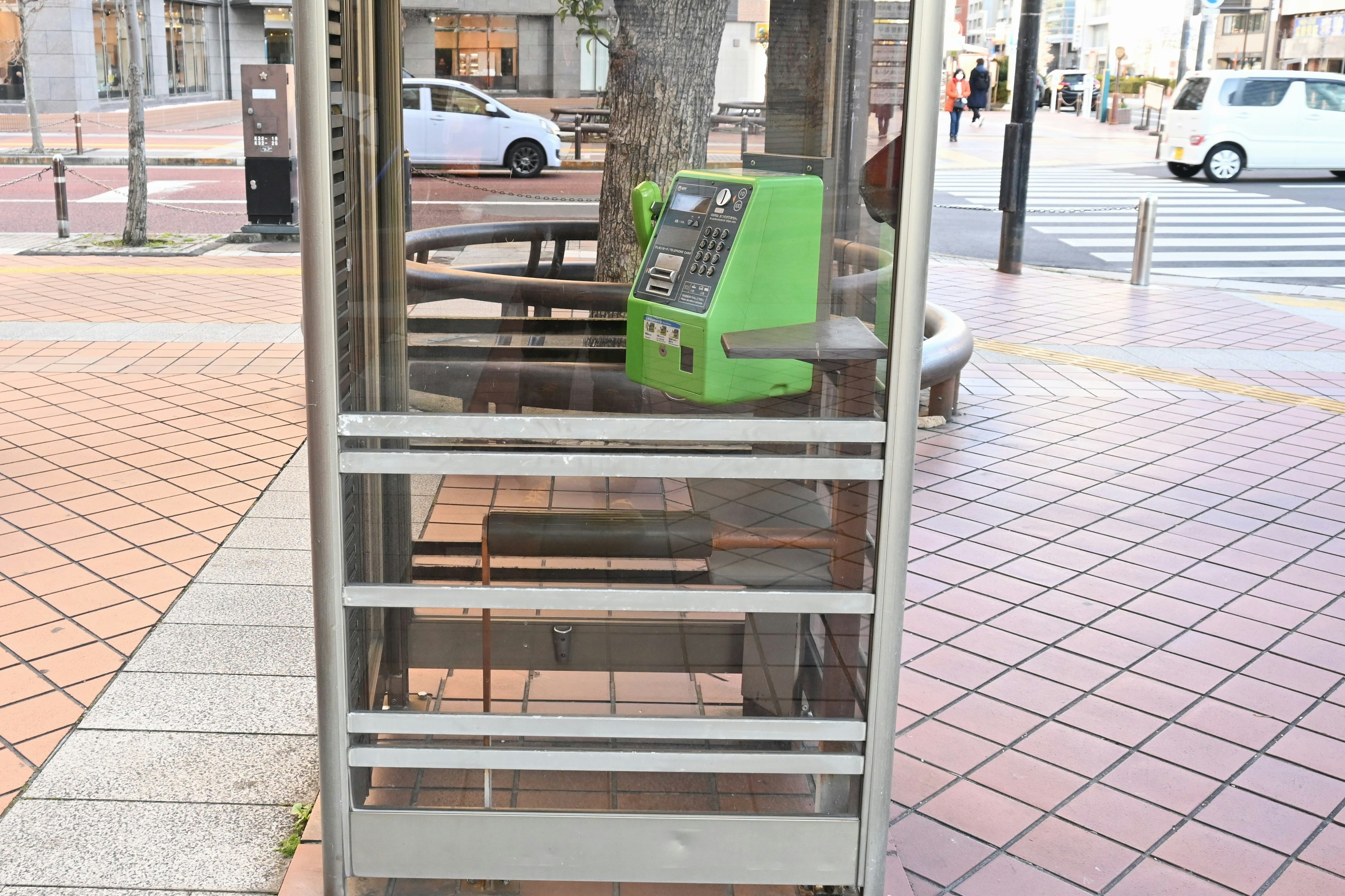 Cabina telefónica transparente con un teléfono verde en una escena callejera