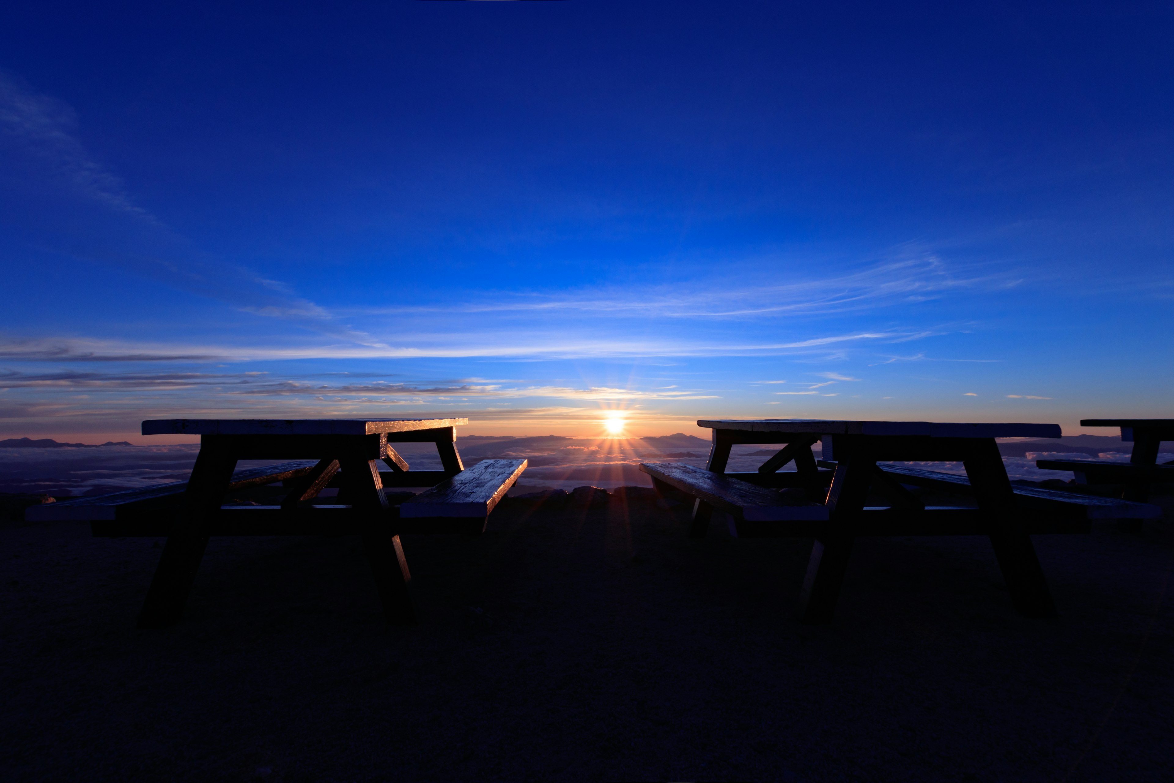 Picknicktische silhouettiert vor einem lebhaften blauen Himmel und Sonnenuntergang