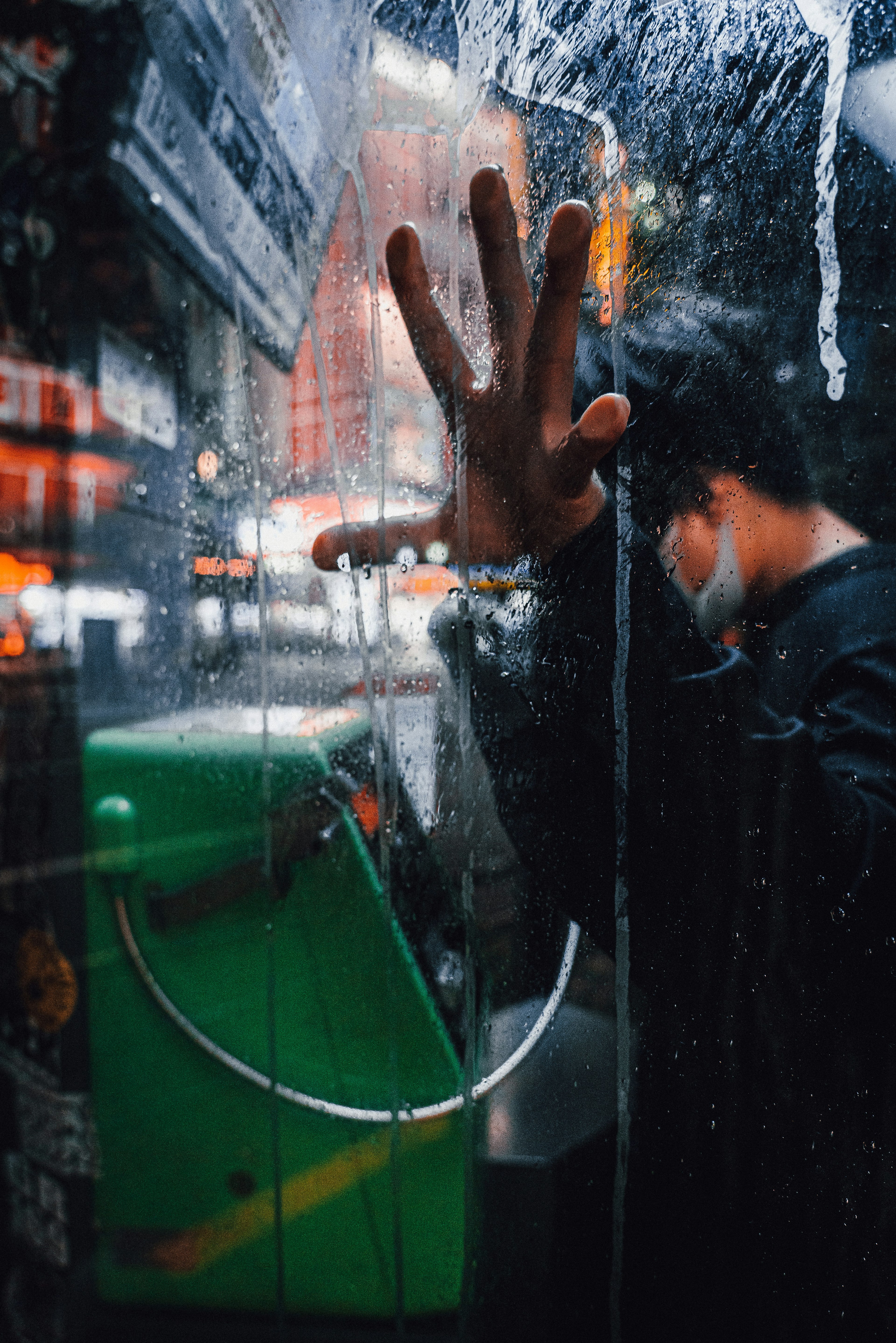 雨に濡れた電話ボックスの中の人の手がガラスに触れている