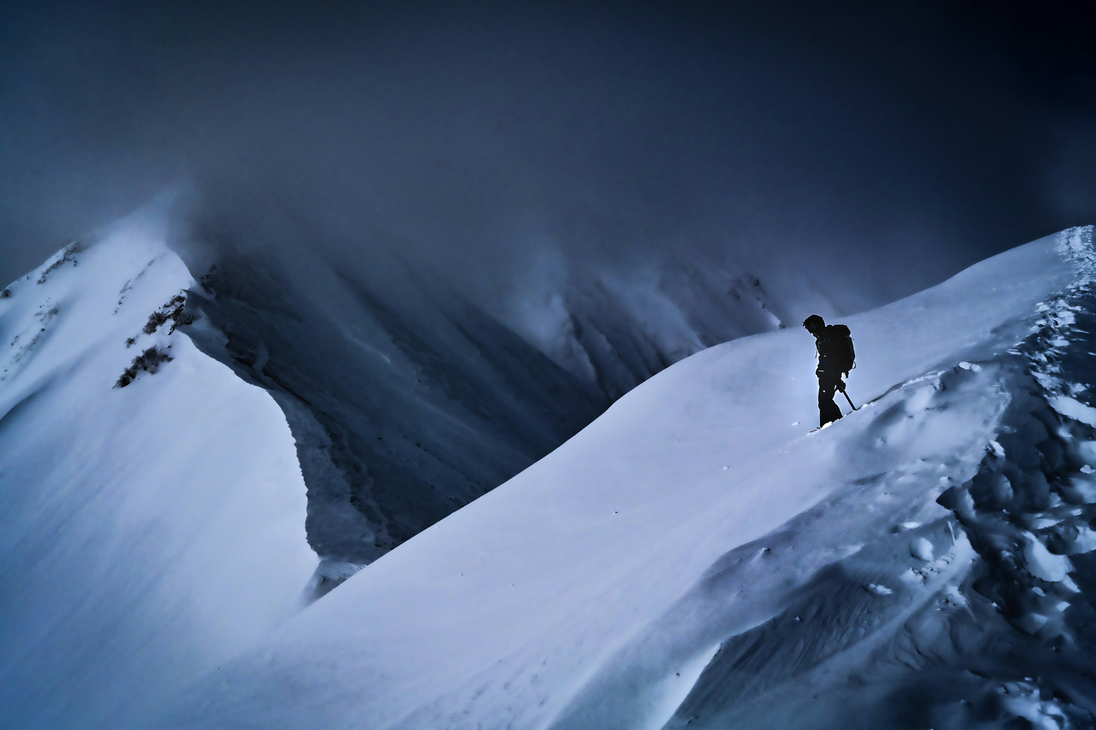 Silhouette of a climber walking on a snow-covered mountain ridge