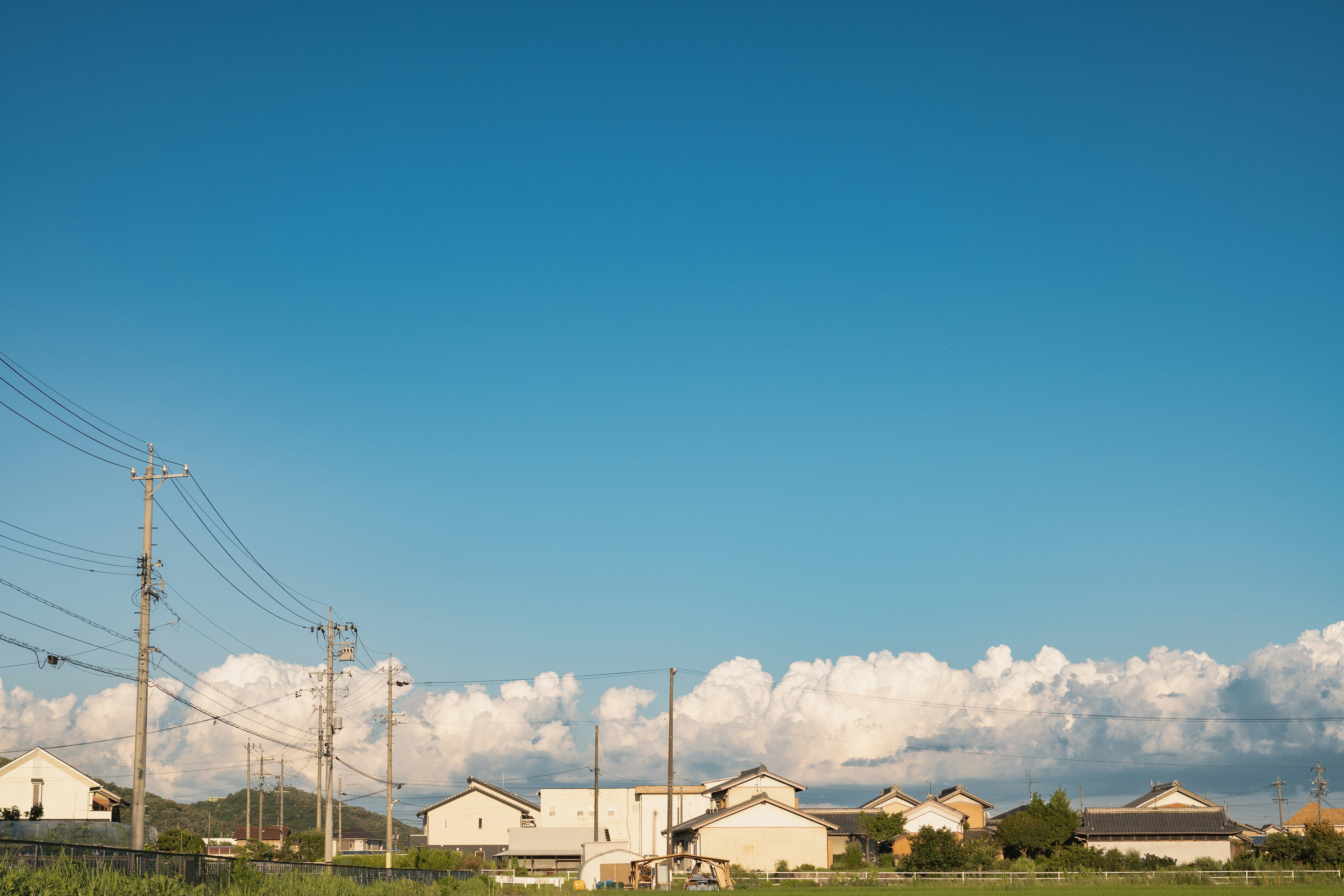 Landschaft mit blauem Himmel und weißen Wolken, die Strommasten und Häuser zeigt