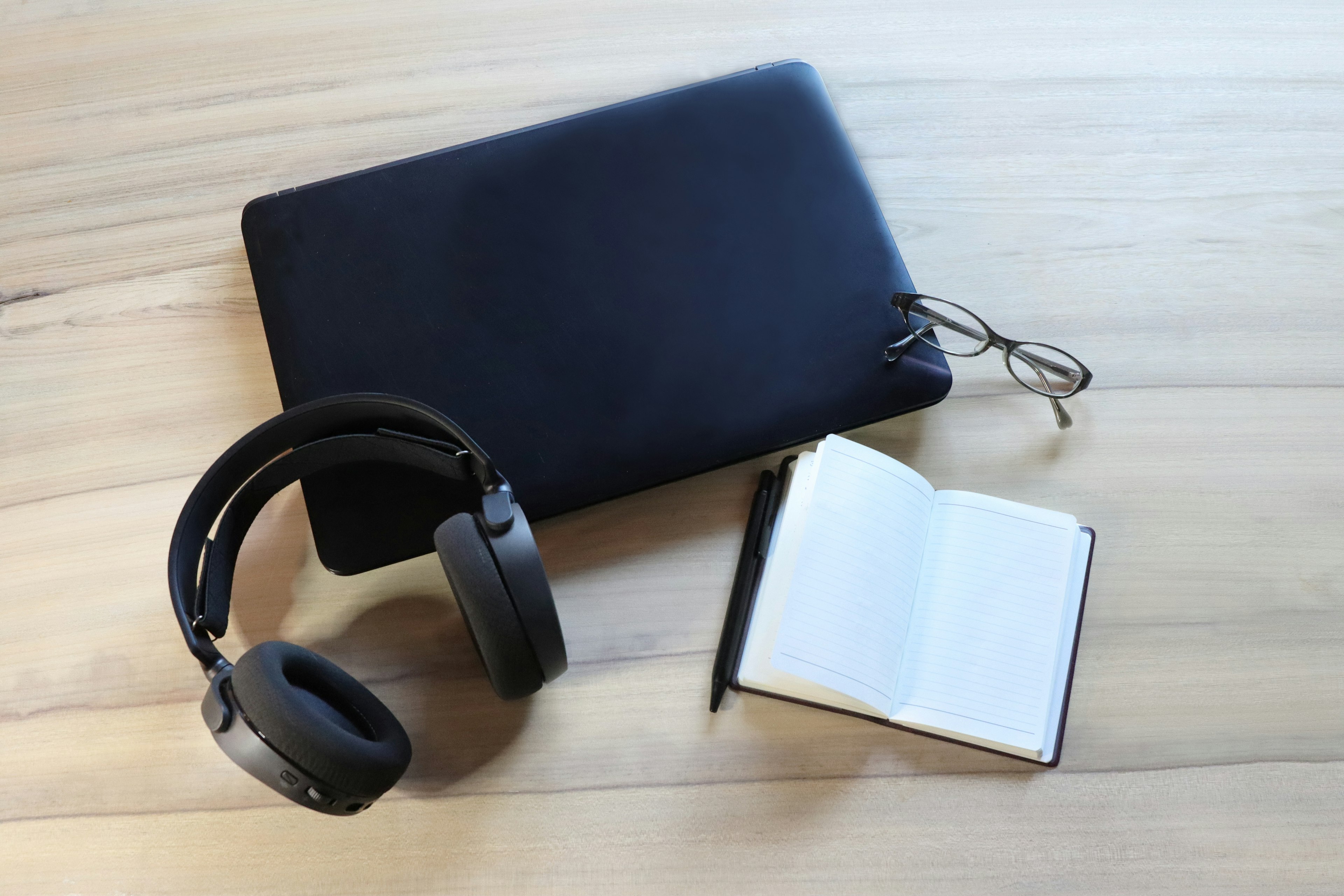 laptop hitam dengan headphone buku catatan dan pena di atas meja kayu