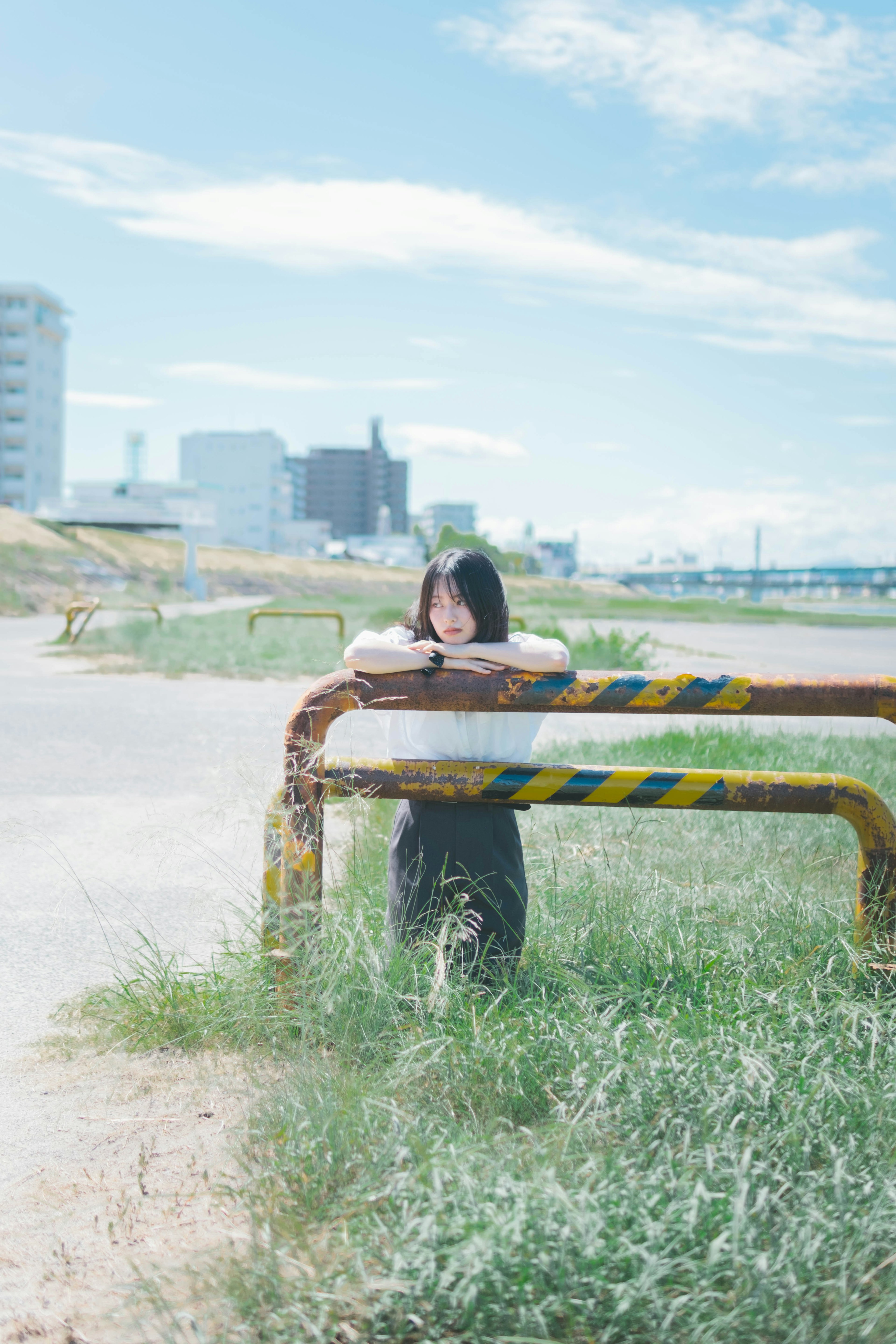 青空の下、古いバリケードに寄りかかる少女と都市の風景