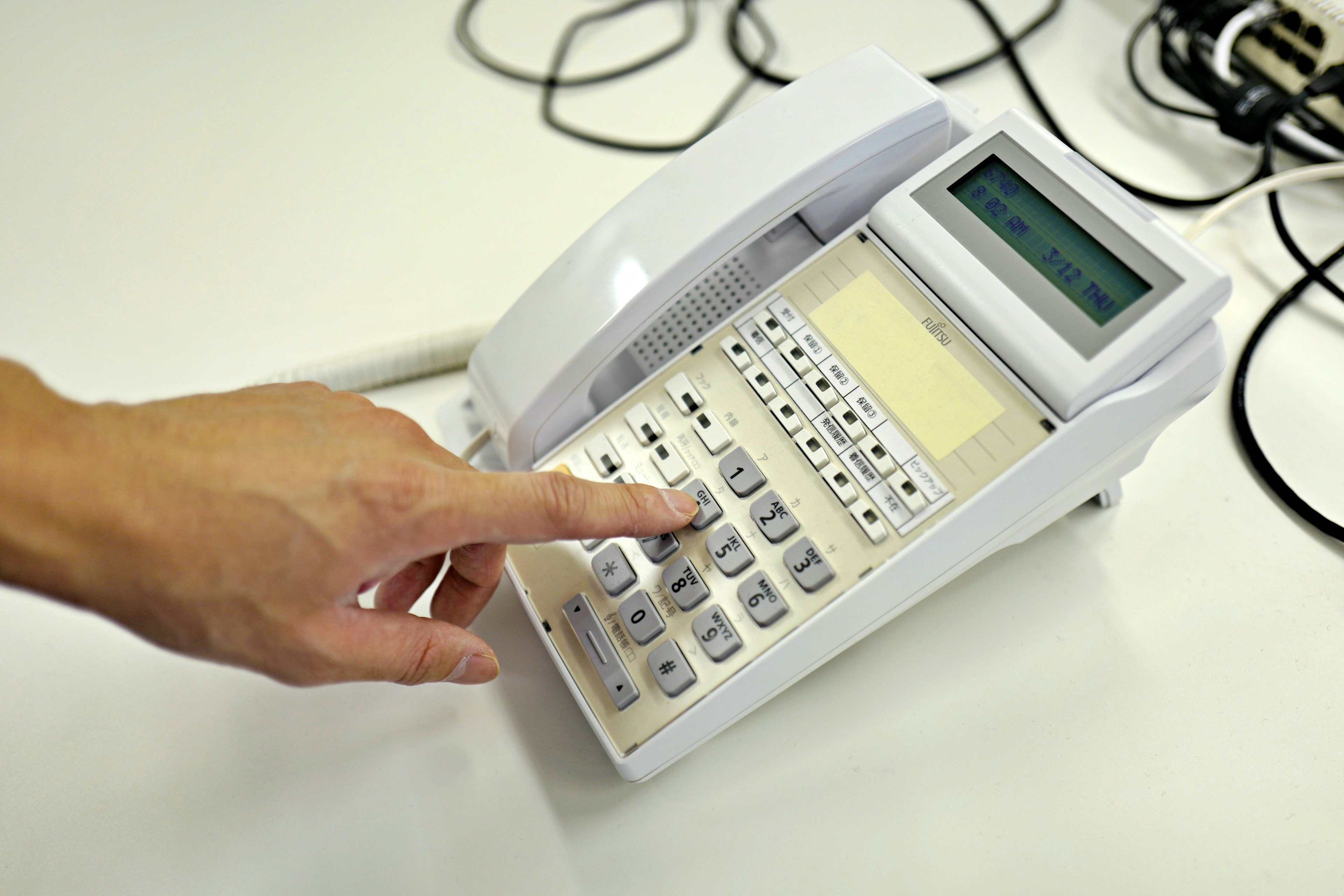 Une main appuyant sur les boutons d'un téléphone blanc