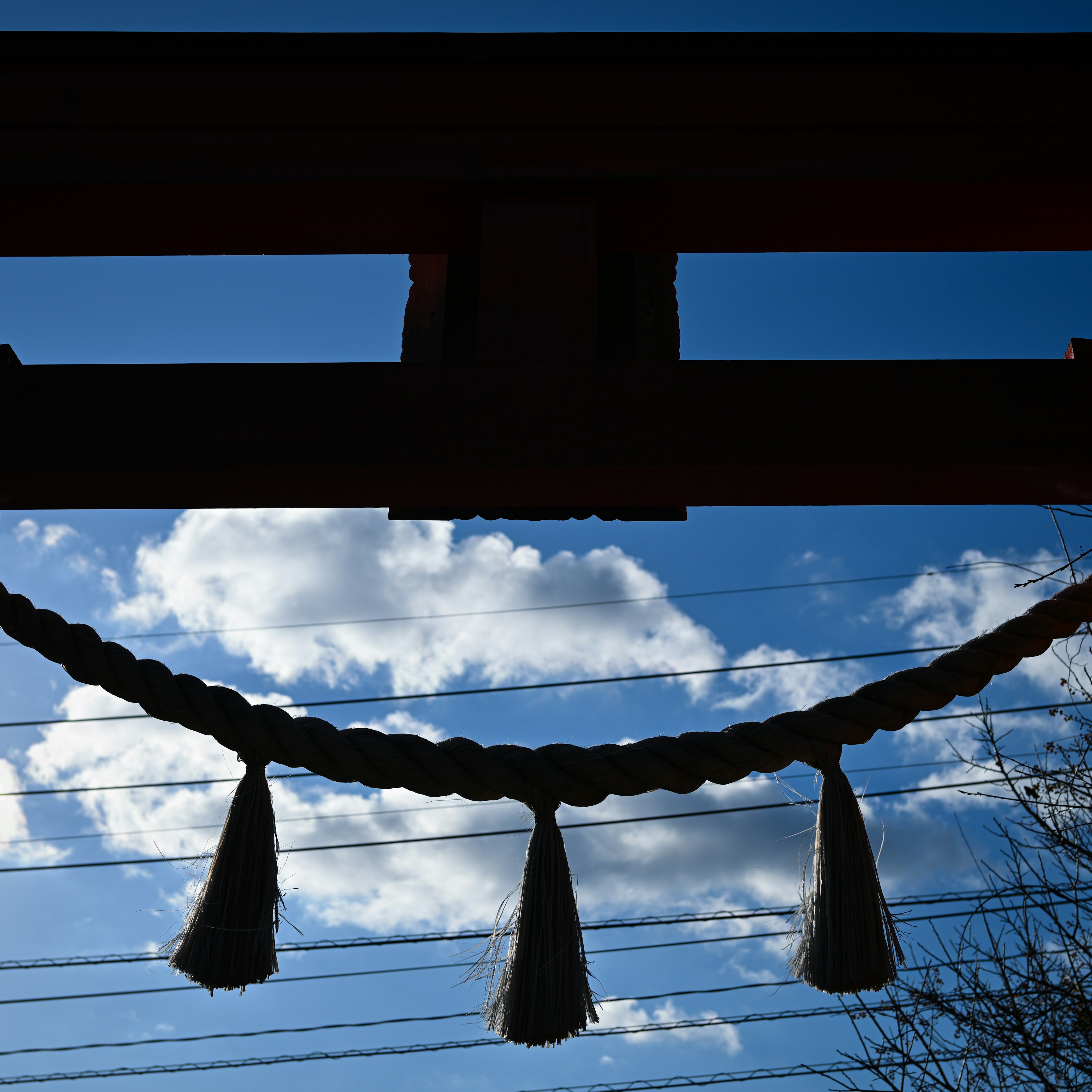 青空と雲が映える神社の鳥居のシルエットに飾られた縄