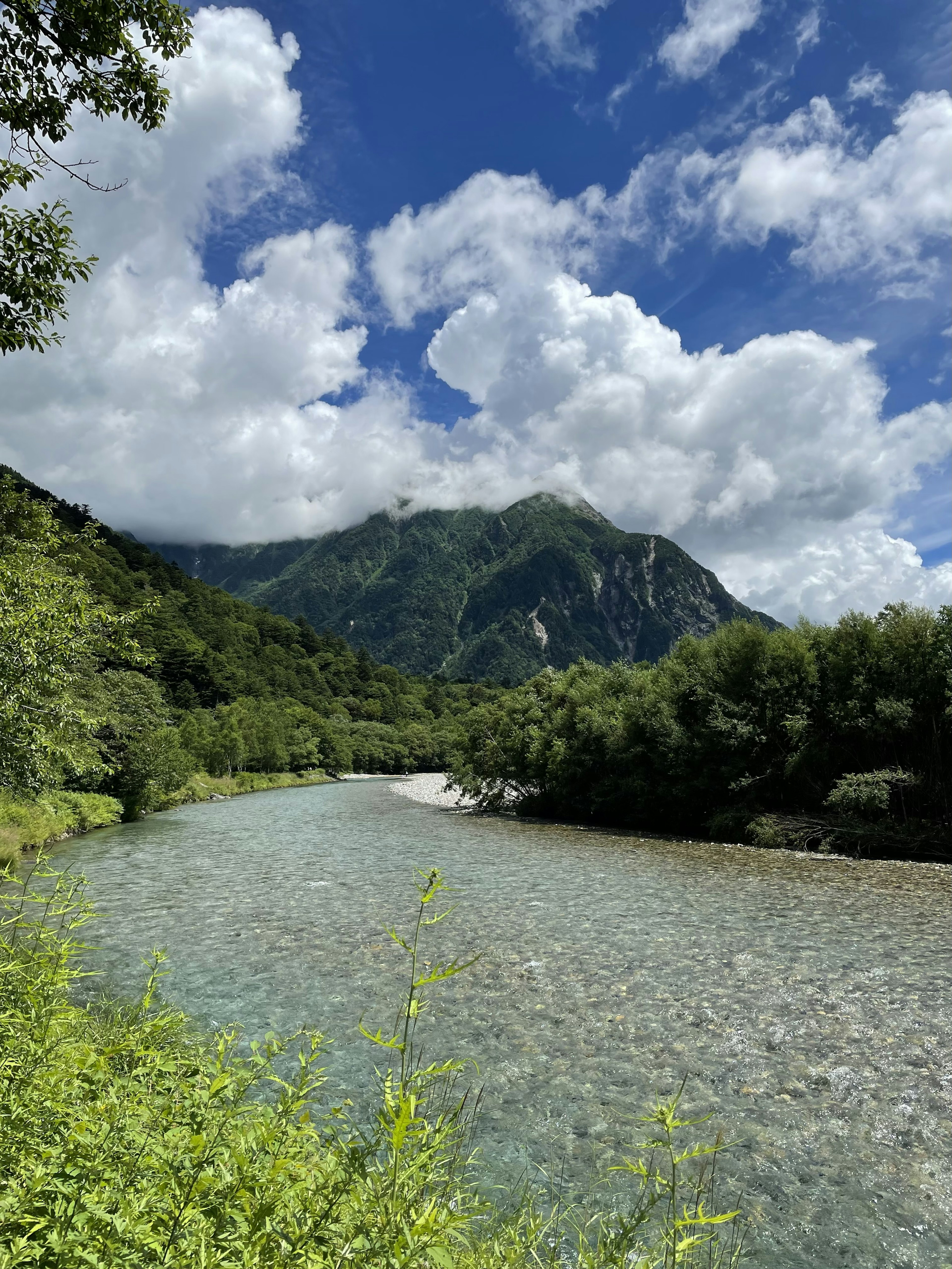 Vue pittoresque d'une rivière claire entourée de montagnes verdoyantes et de nuages