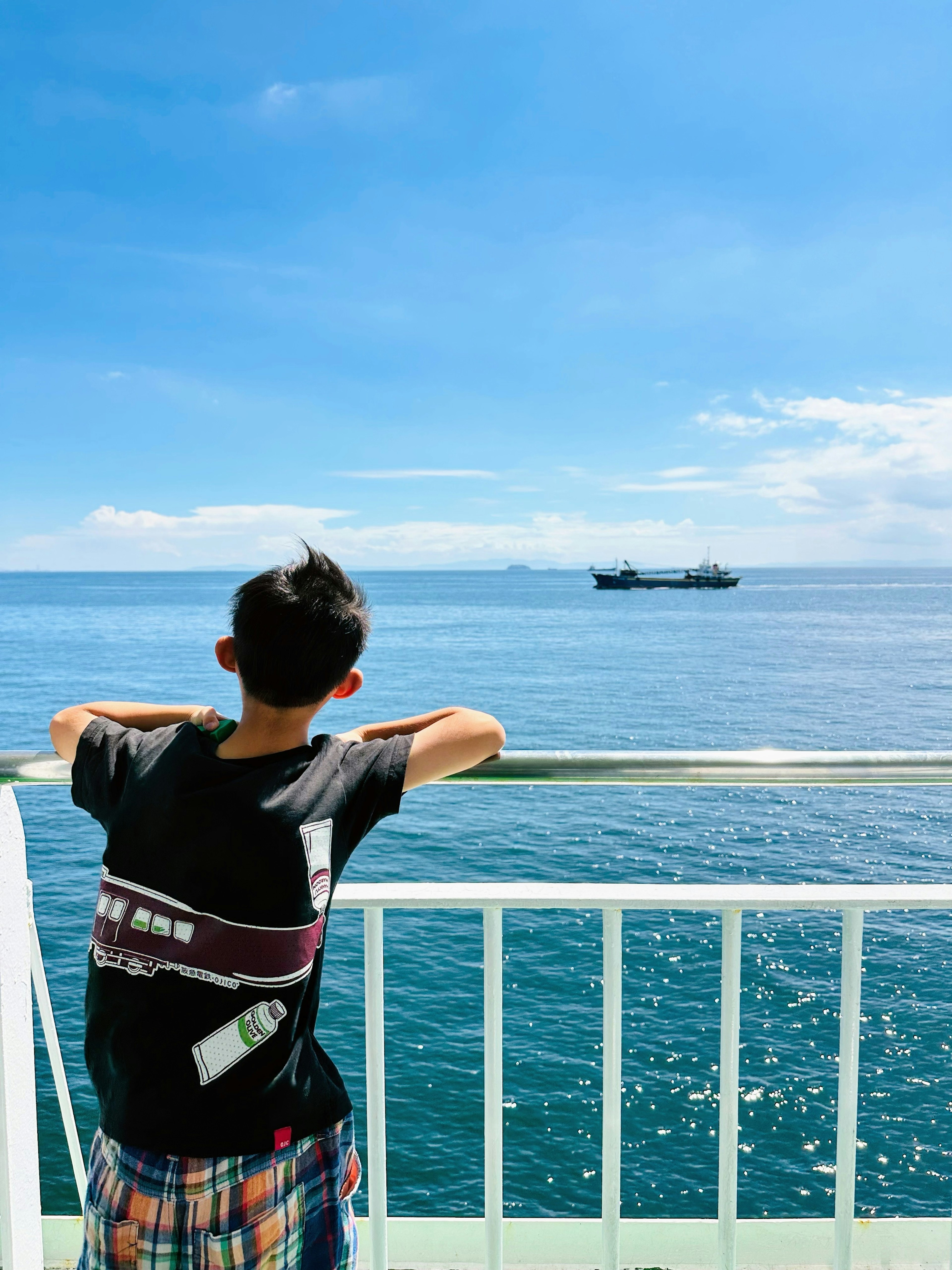 Seorang anak laki-laki yang melihat laut dengan kapal dan langit biru di latar belakang