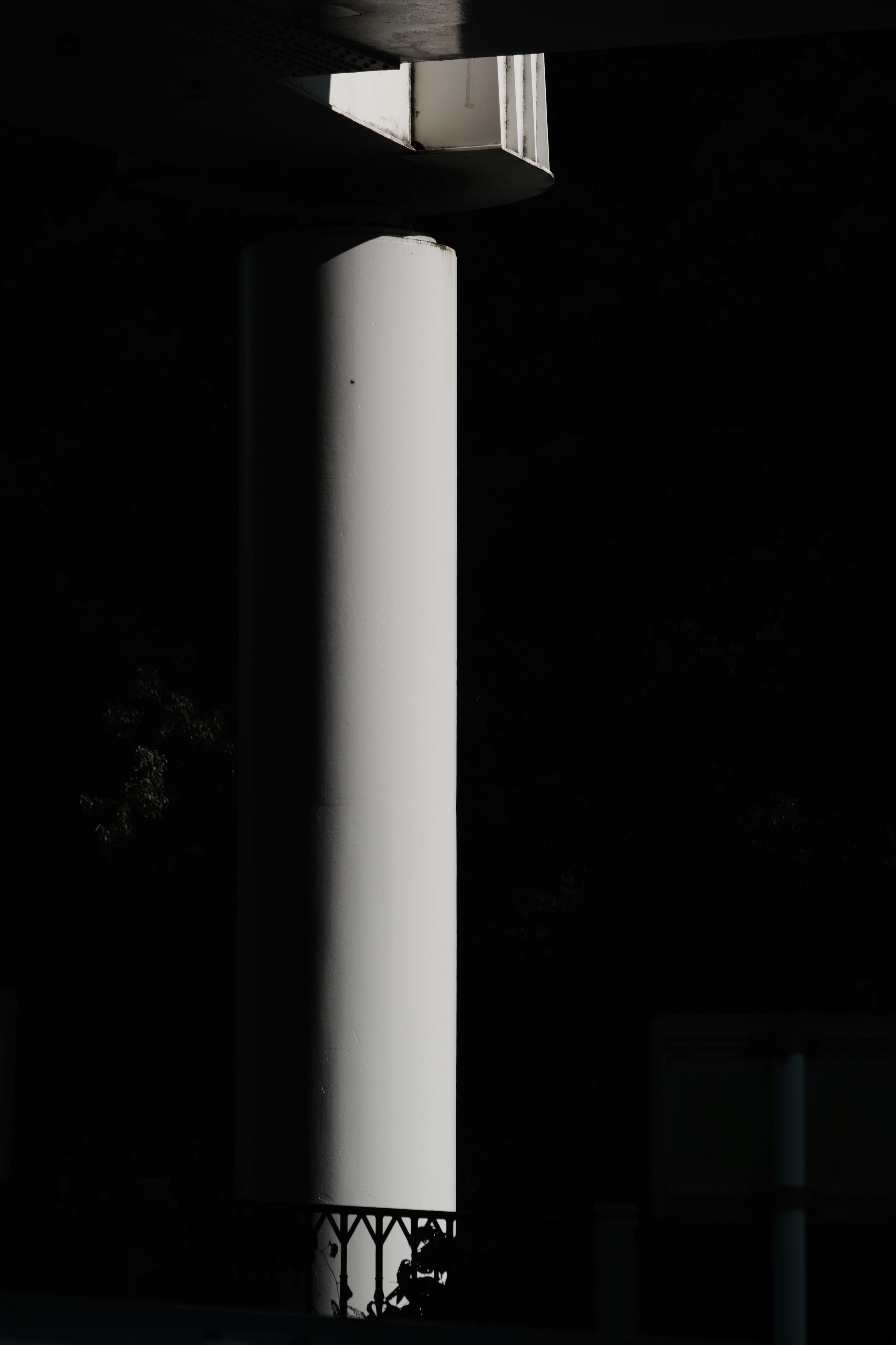 A tall white column with intricate base in shadowy background