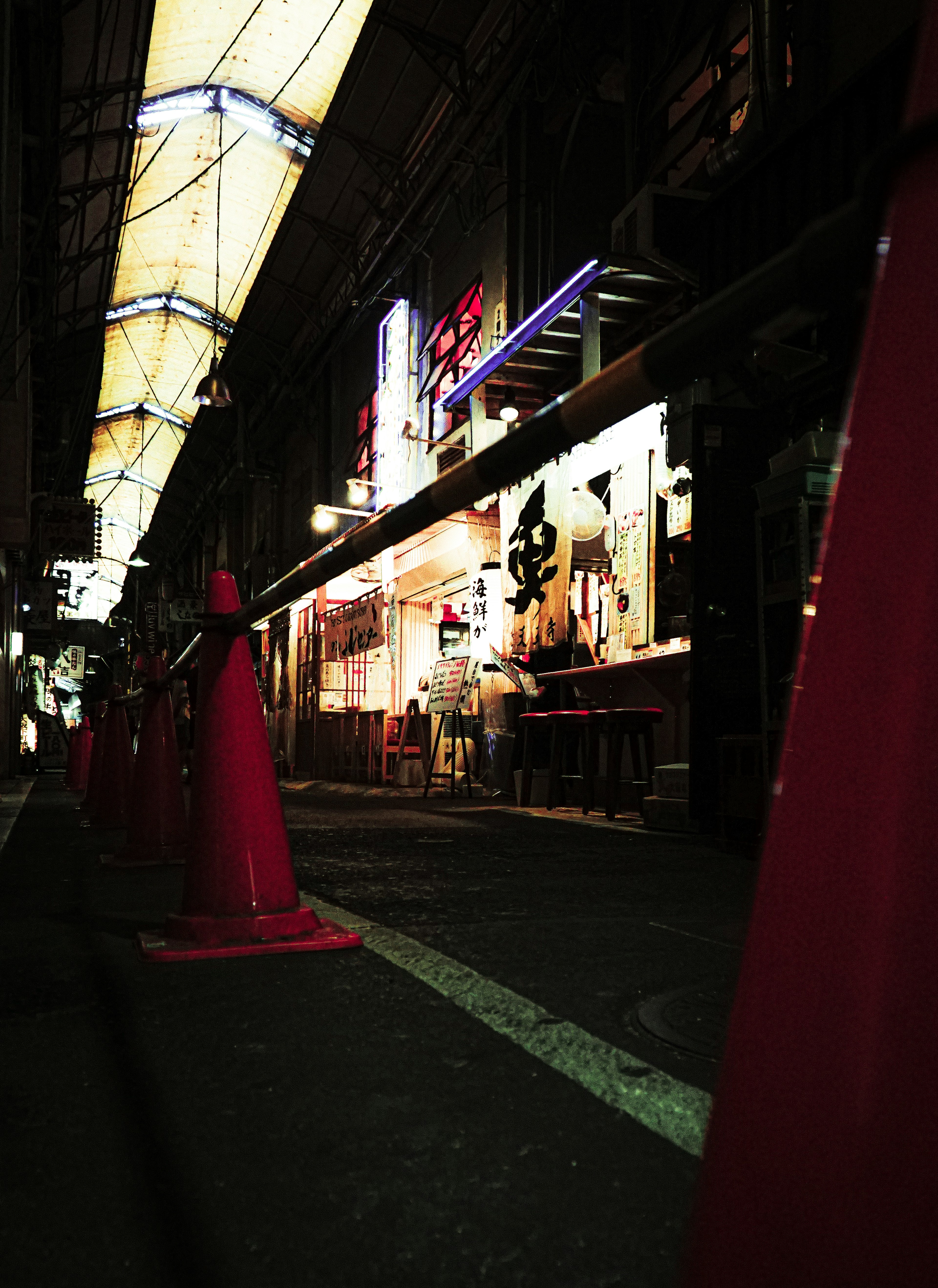 Dark street with red cones and brightly lit shop signs