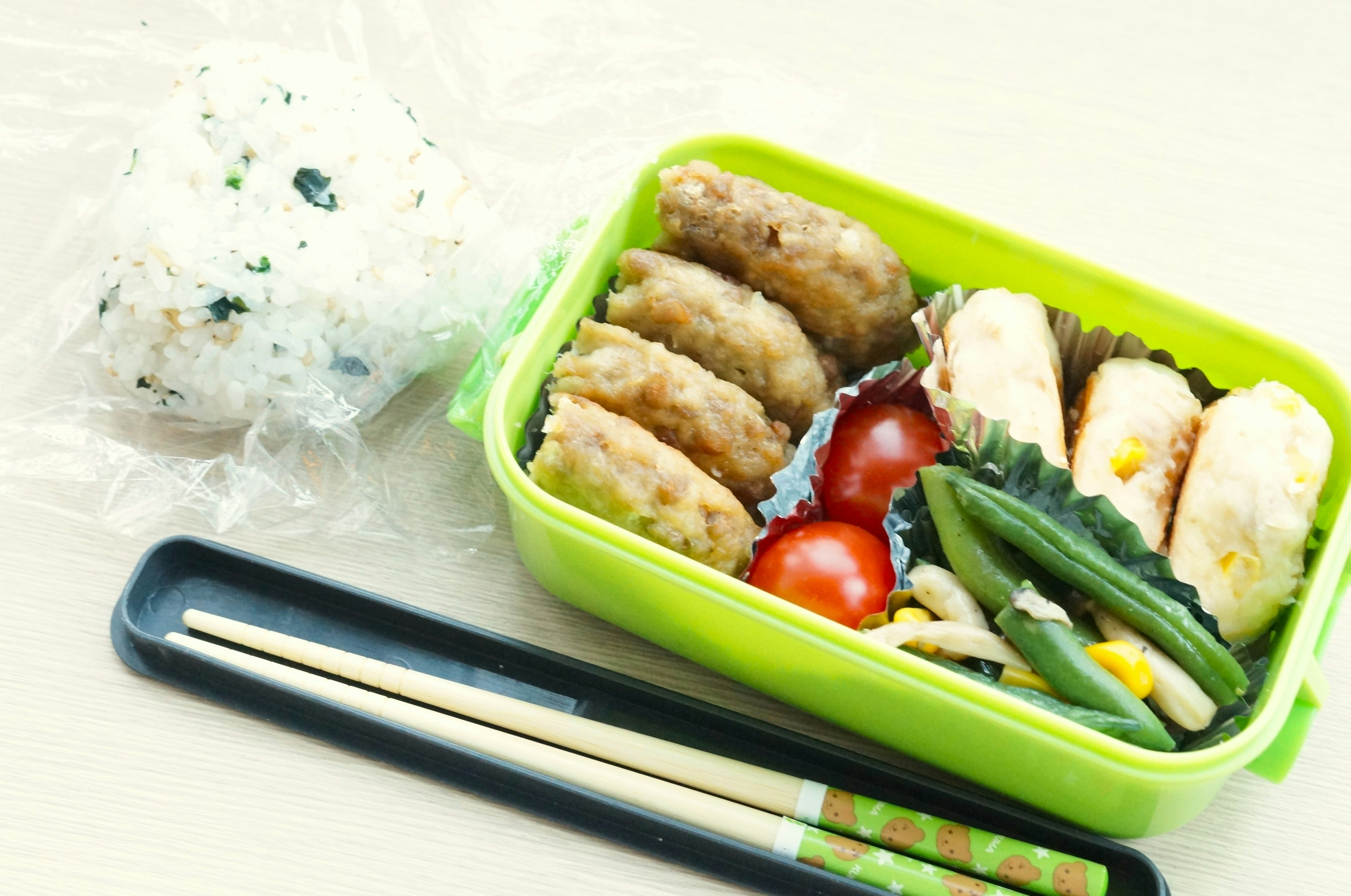 Une boîte à bento verte remplie d'articles frits et de légumes avec des boules de riz