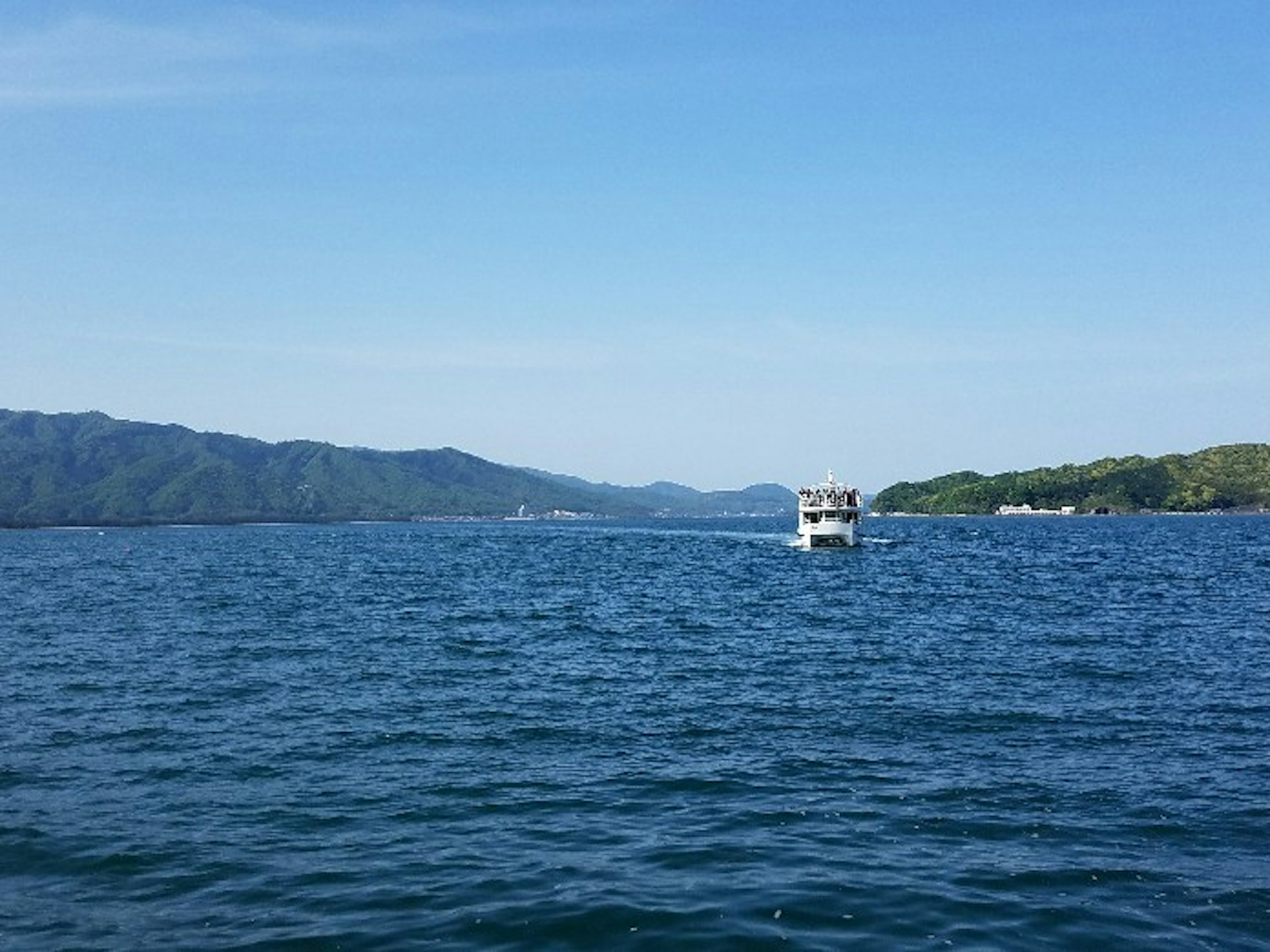 Mar tranquilo con un barco cielo azul y montañas a lo lejos