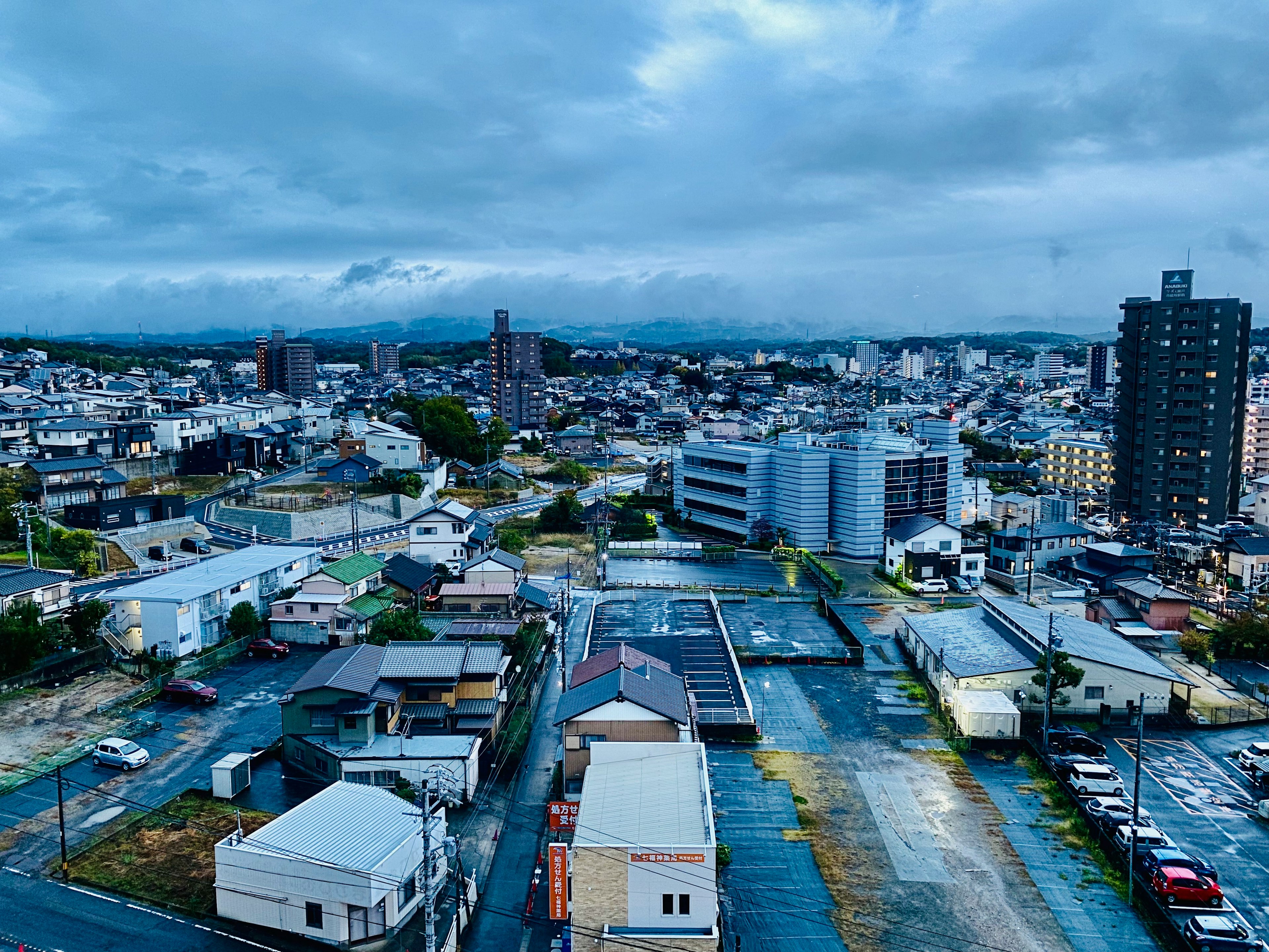 都市の夜景、ビルと住宅が並ぶ風景、曇り空と山のシルエット