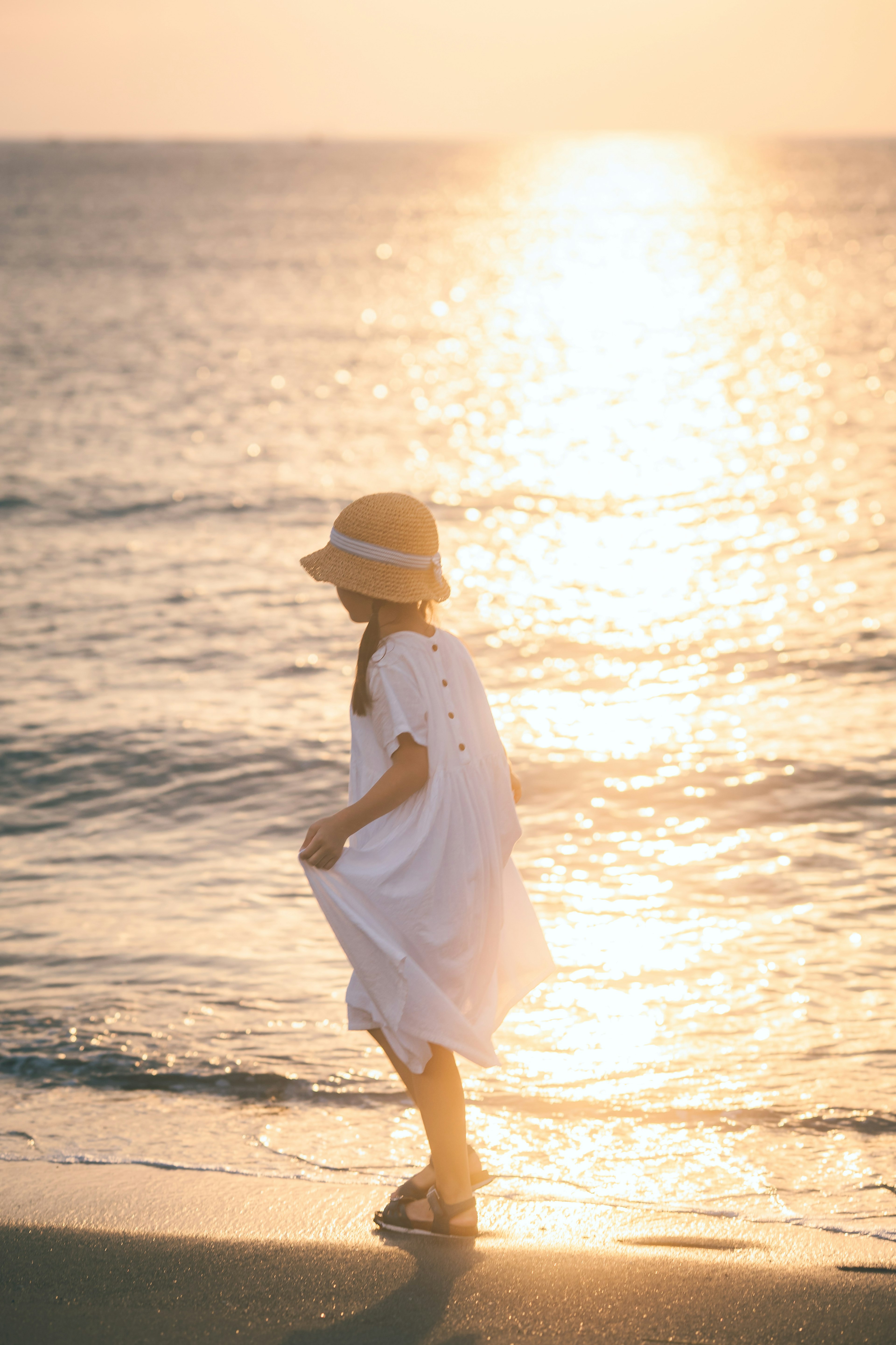 Una ragazza in abito bianco che cammina sulla spiaggia con il tramonto sullo sfondo