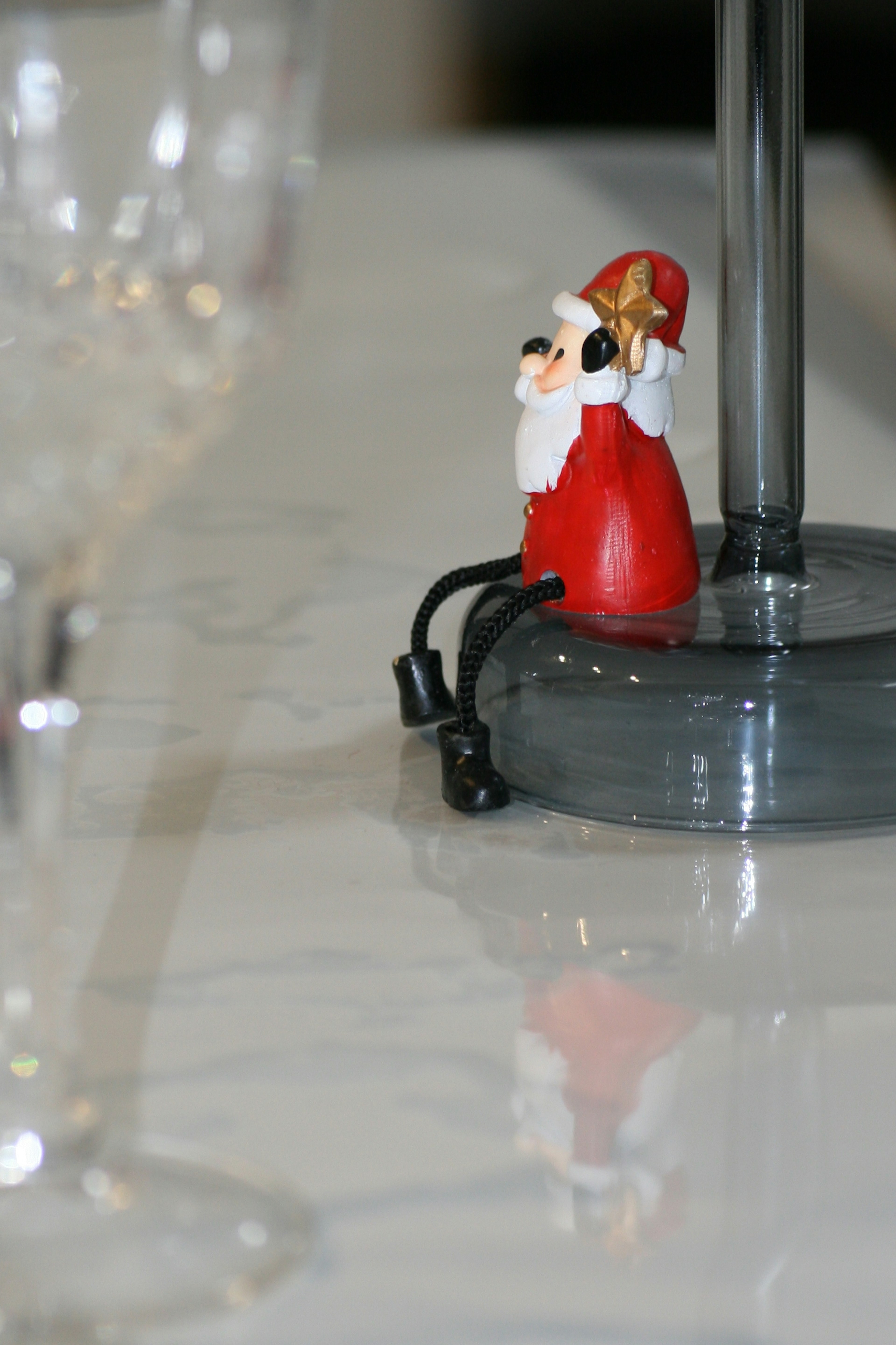 Kleine Weihnachtsmann-Figur auf einem Tisch mit einem Glas im Vordergrund