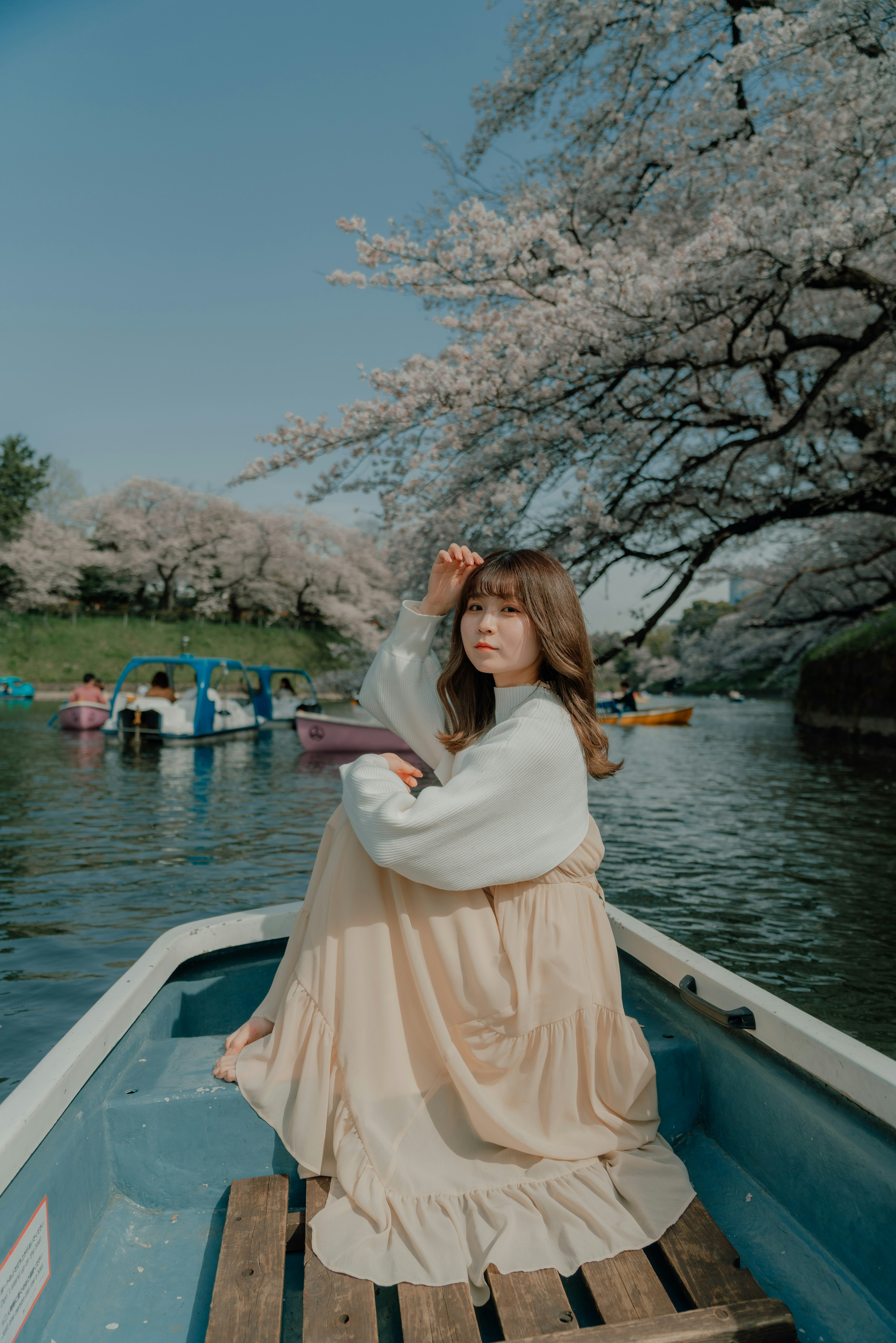 Femme en vêtements doux assise dans un bateau sous des cerisiers en fleurs