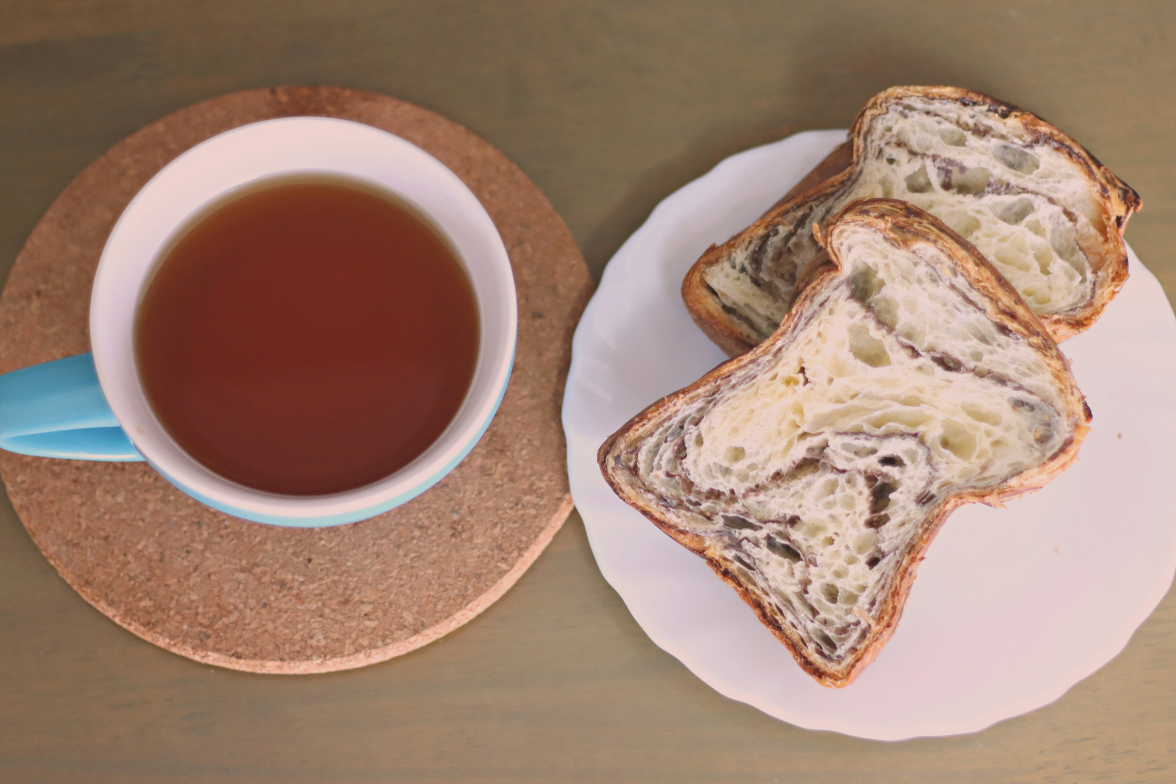 Sliced bread on a white plate next to a cup of tea on a cork coaster