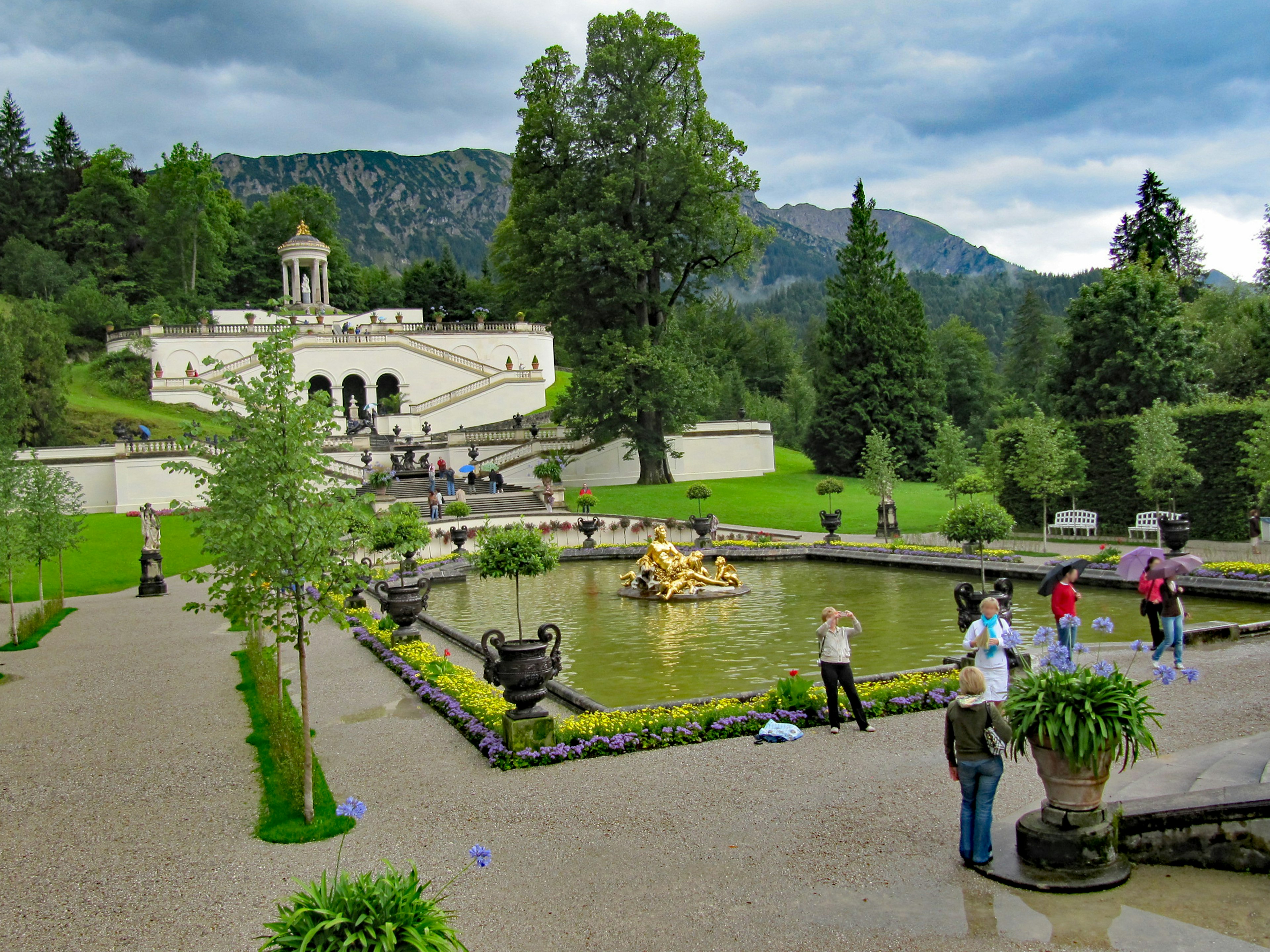 Scenic garden with visitors and a pond lush greenery and mountains in the background