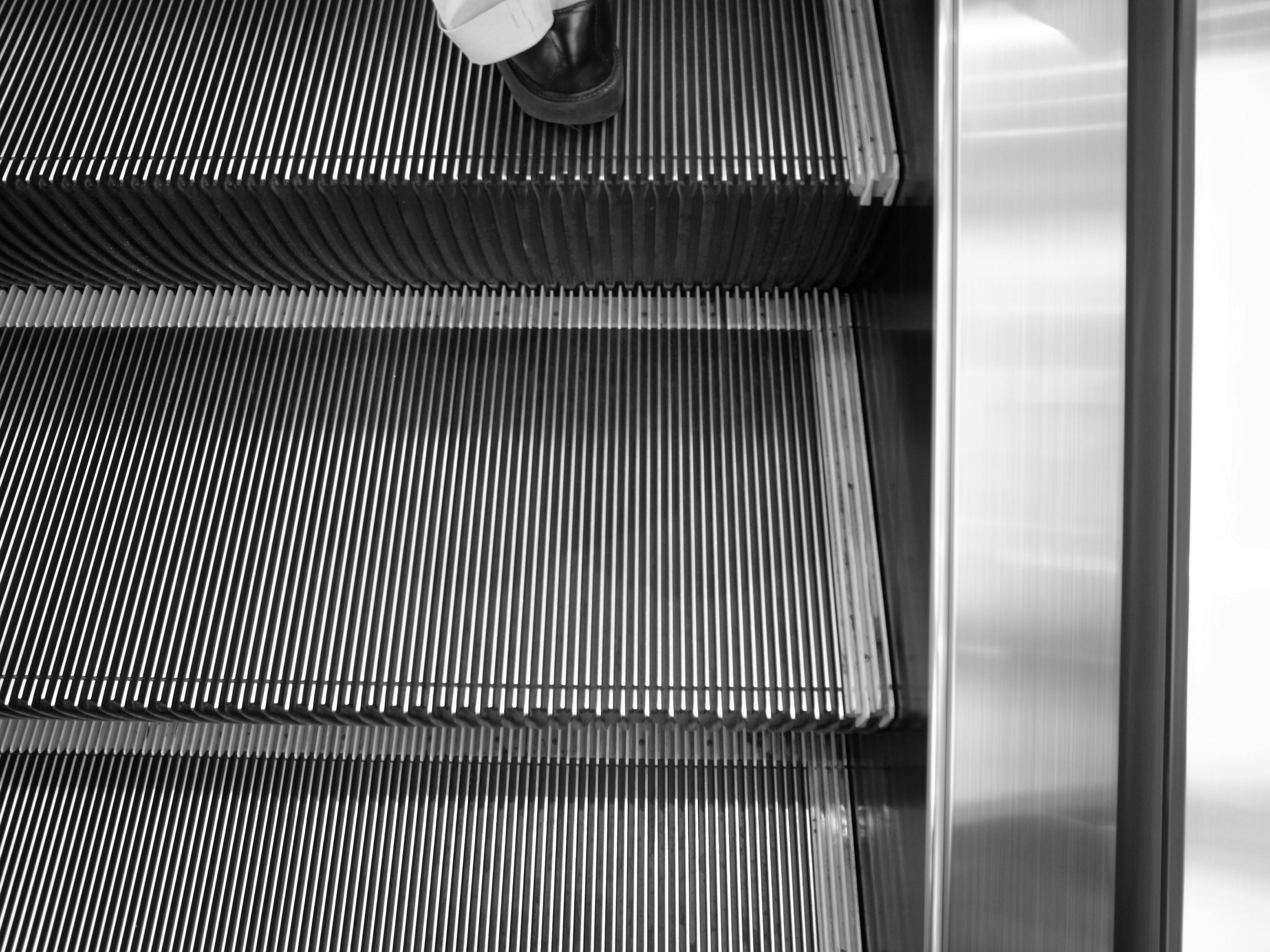 Black and white image of escalator metal steps and part of the handrail