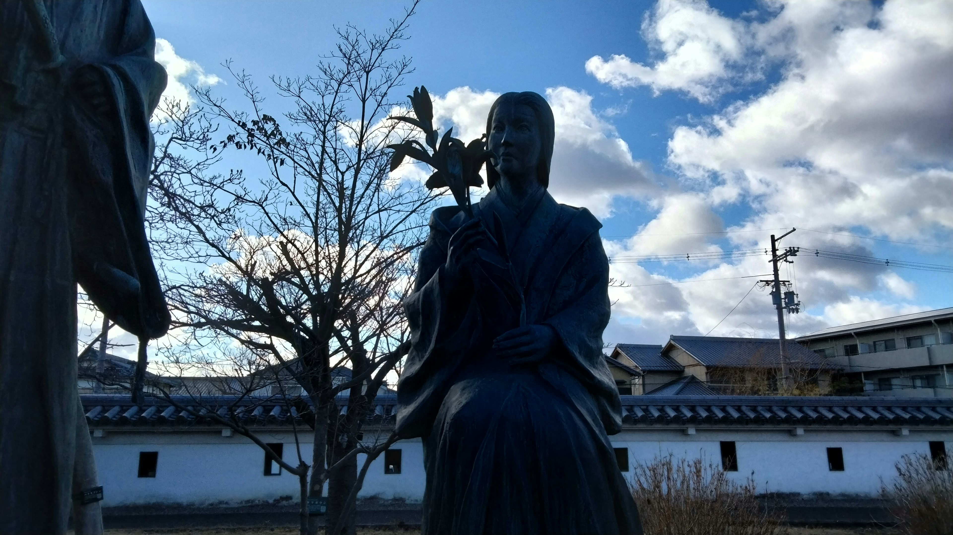 Statue holding a flower under a blue sky with buildings in the background