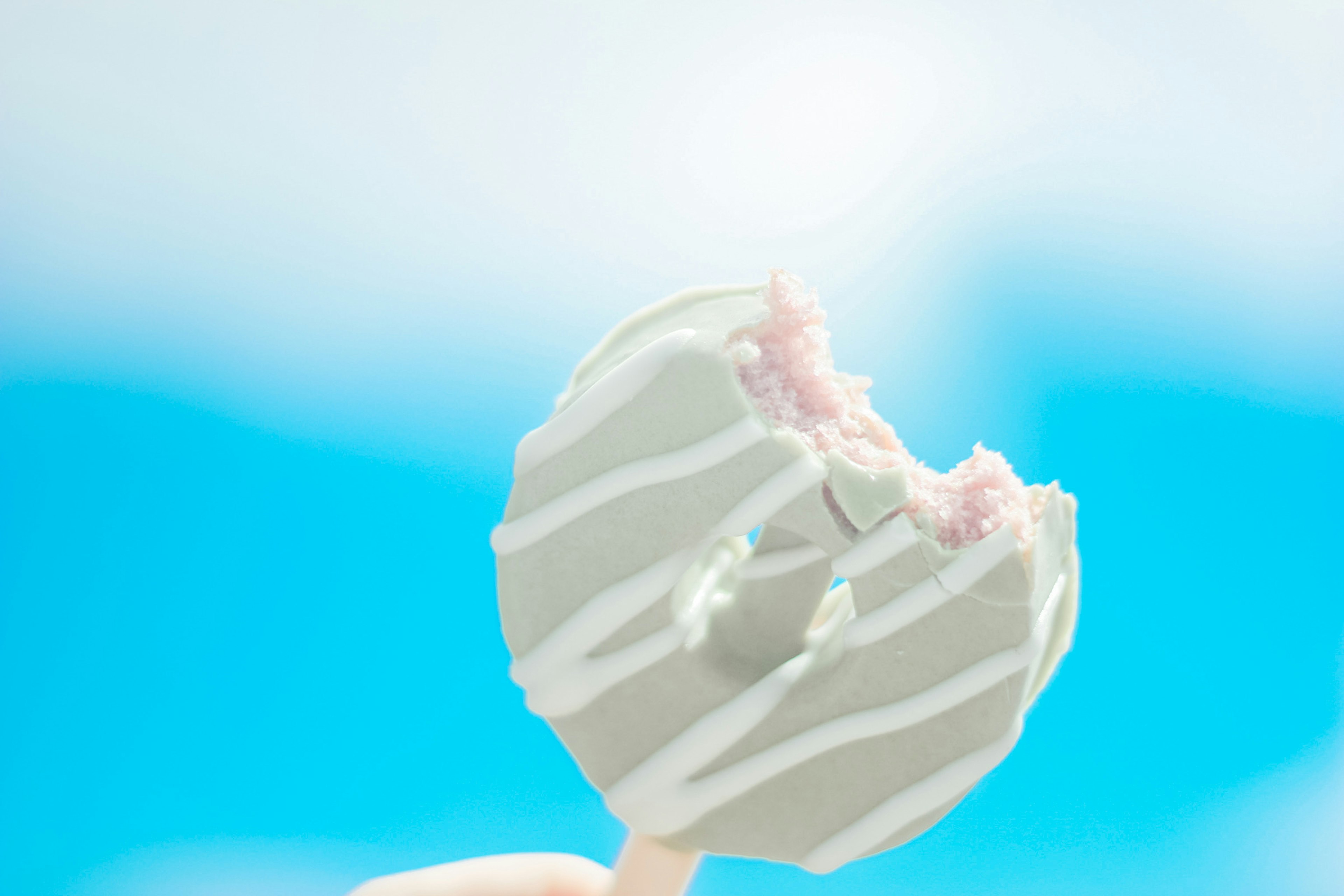 A bitten white chocolate-coated ice pop against a blue sky background