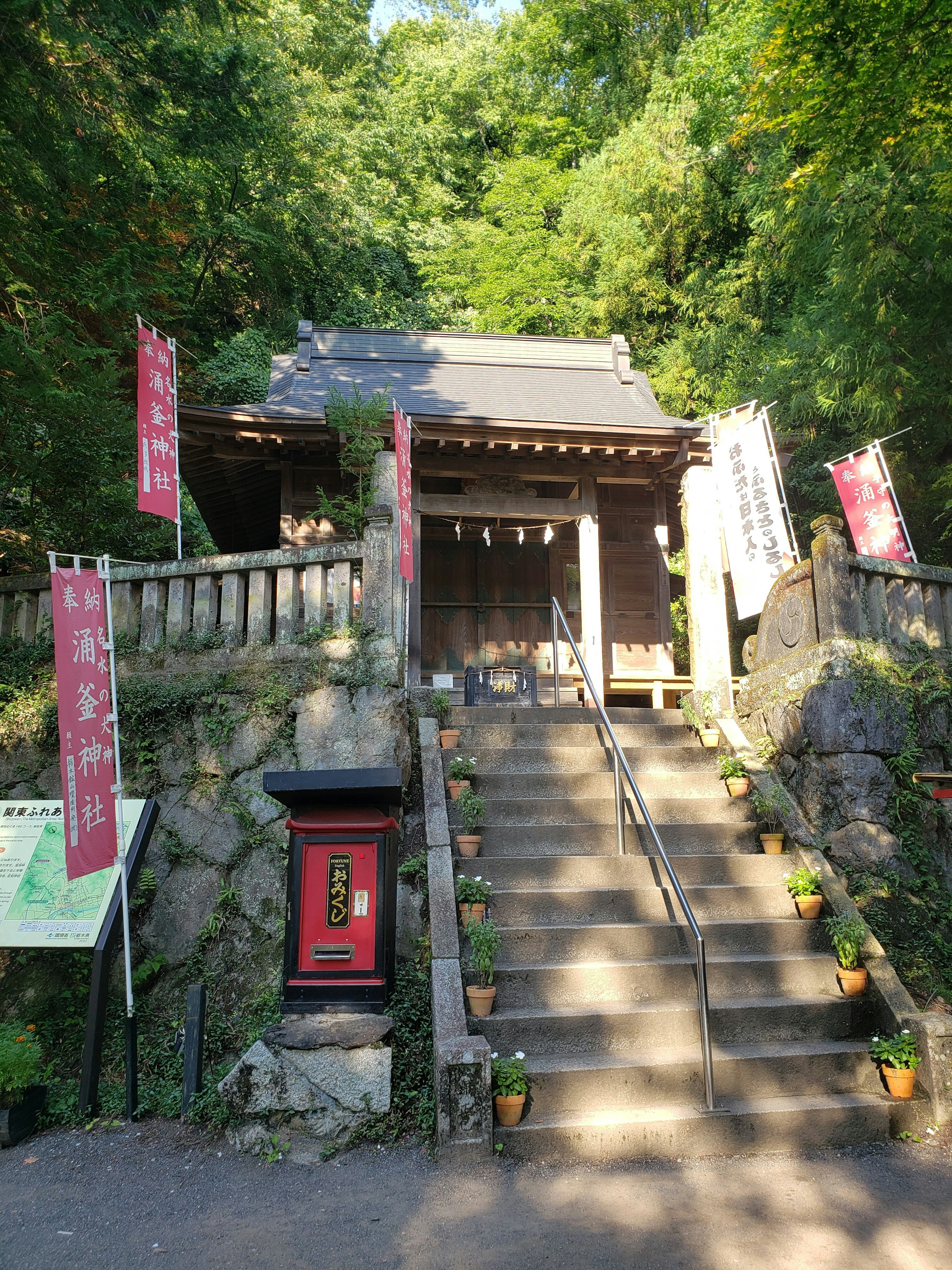 Entrance of a traditional Japanese shrine with steps leading up surrounded by greenery