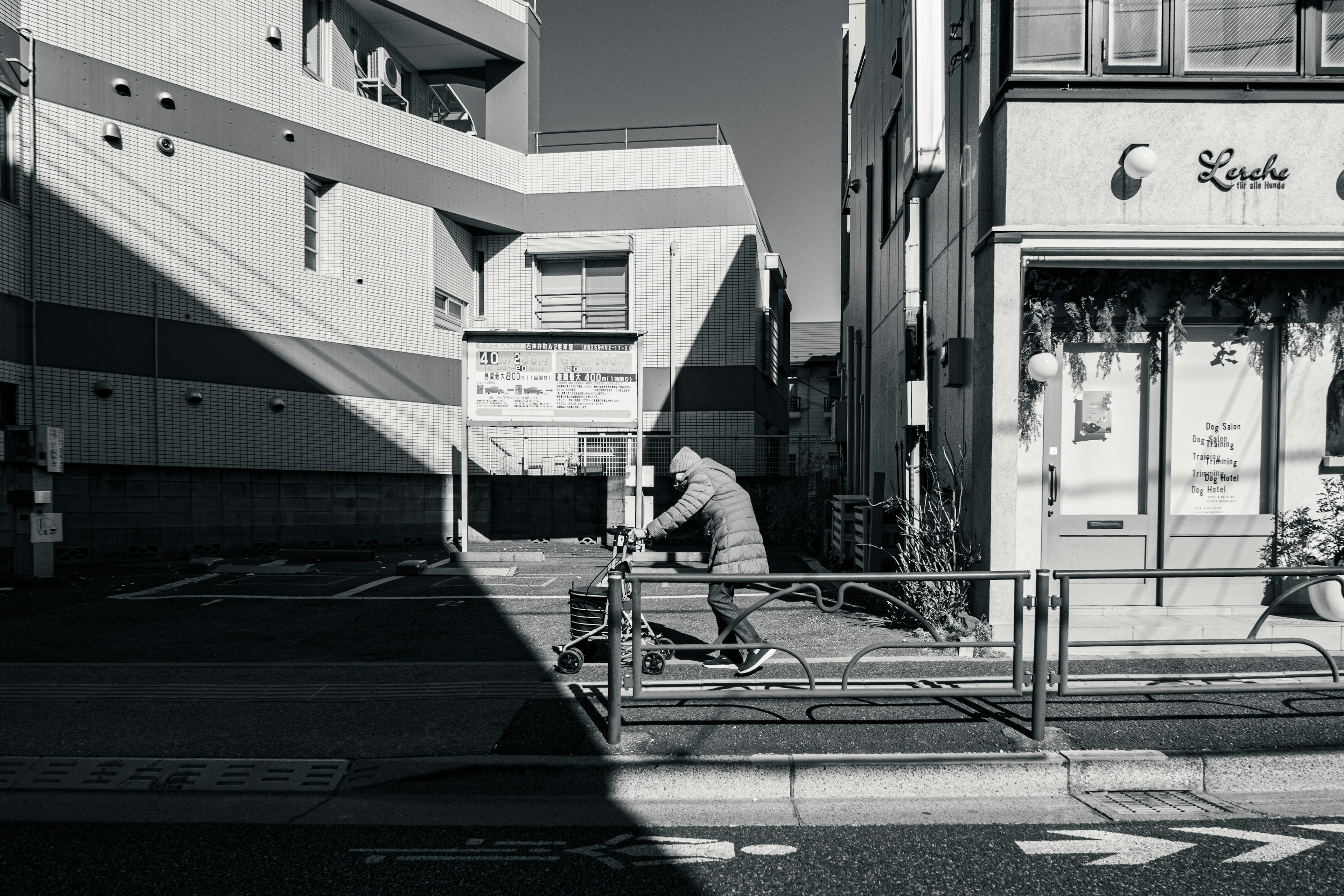 A person walking on a street corner in black and white A large shadow cast by a building