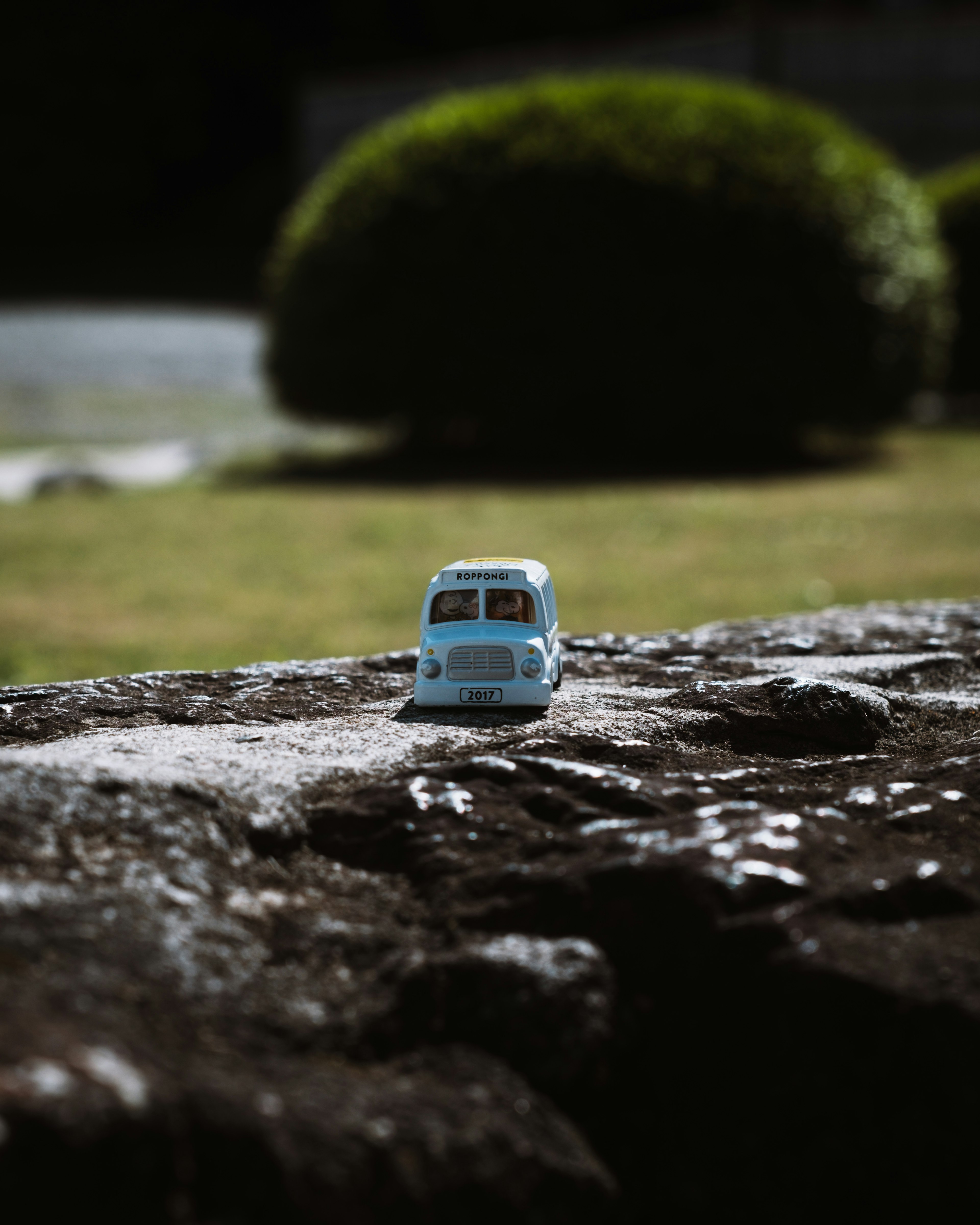 A blue toy car placed on a rock with a blurred background