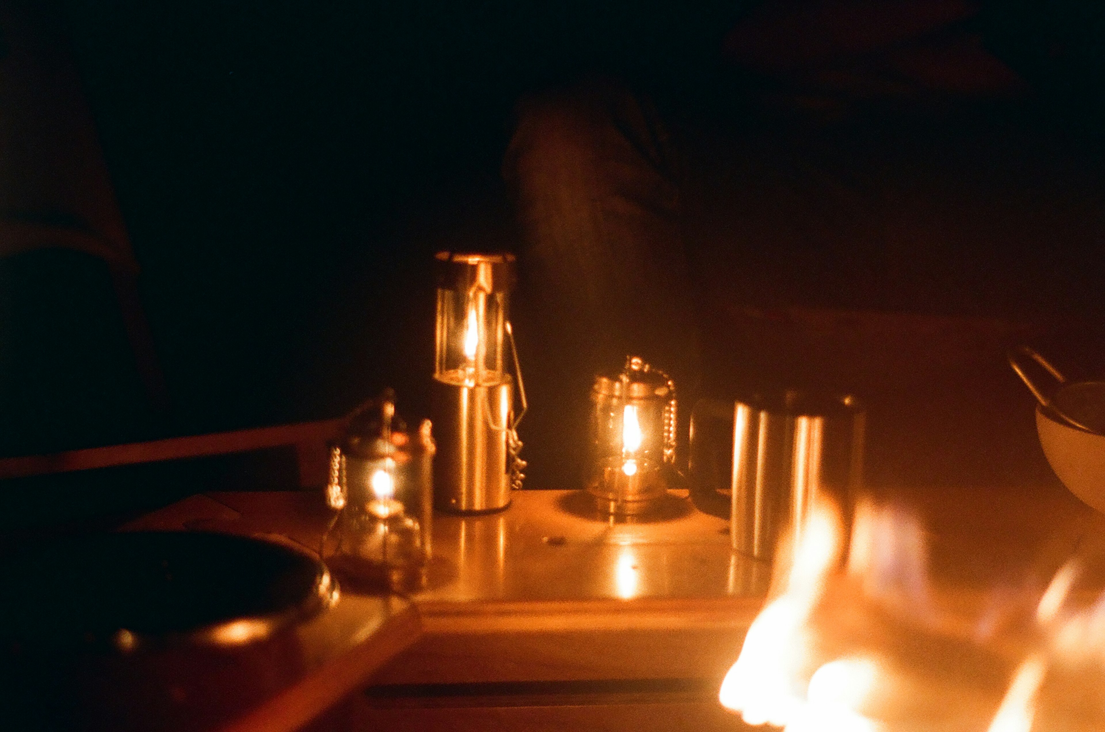 A cozy table scene with camping lanterns and a warm fire in a dark setting