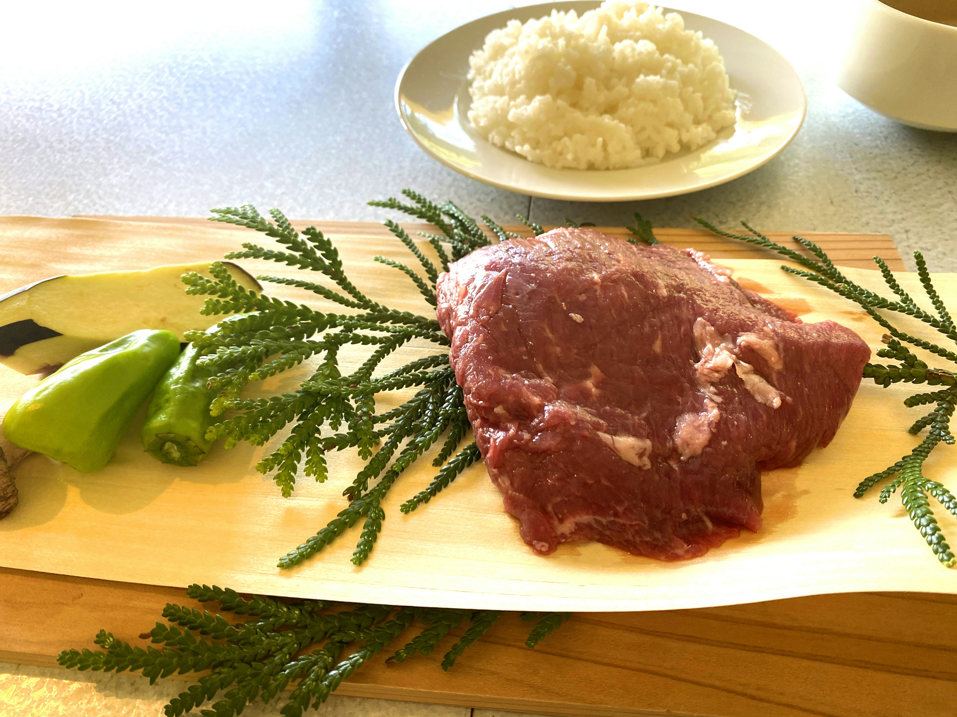 Carne fresca e verdure disposte su un piatto con riso sullo sfondo