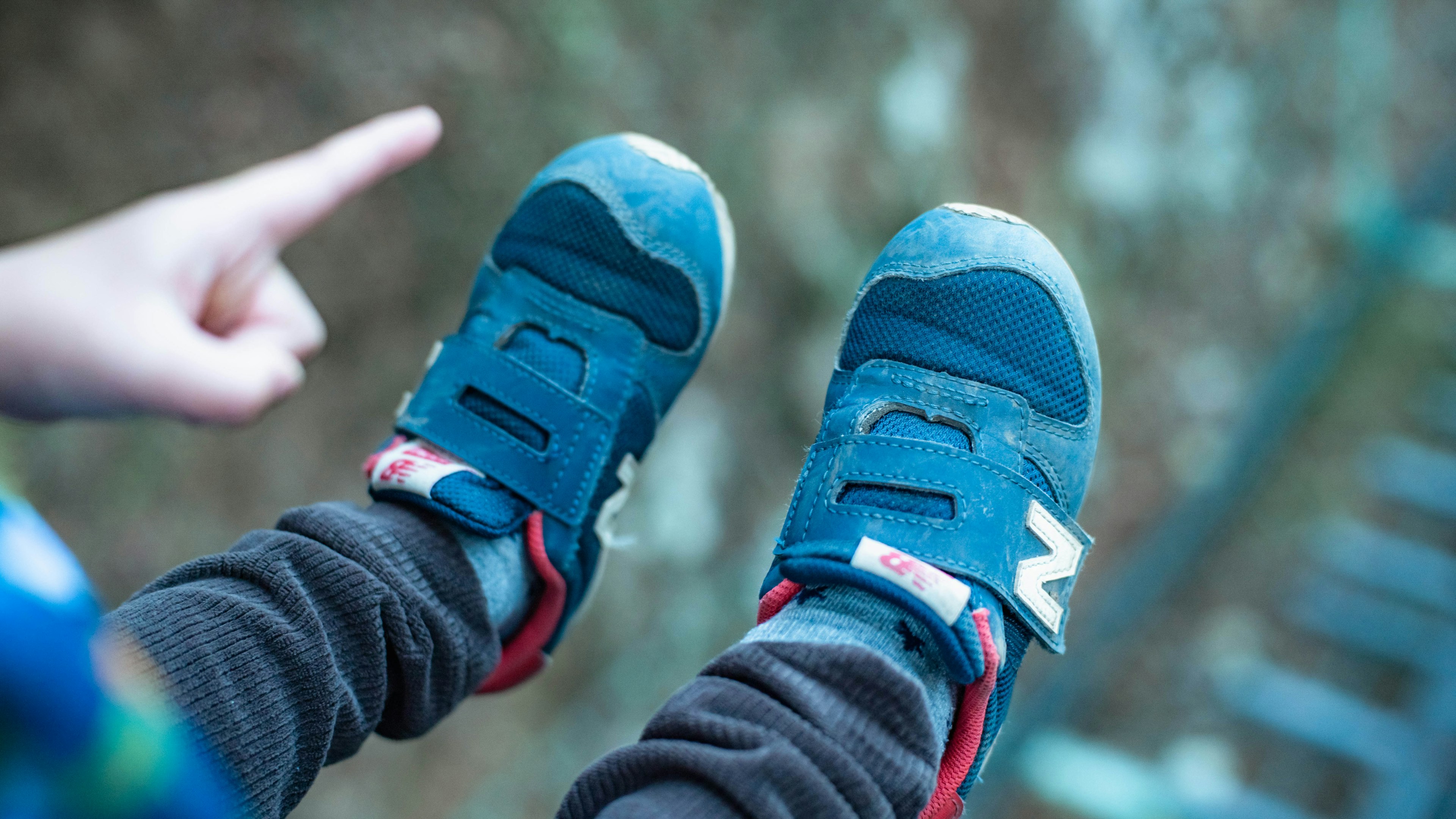 Piedi di bambino in scarpe da ginnastica blu con una mano che punta