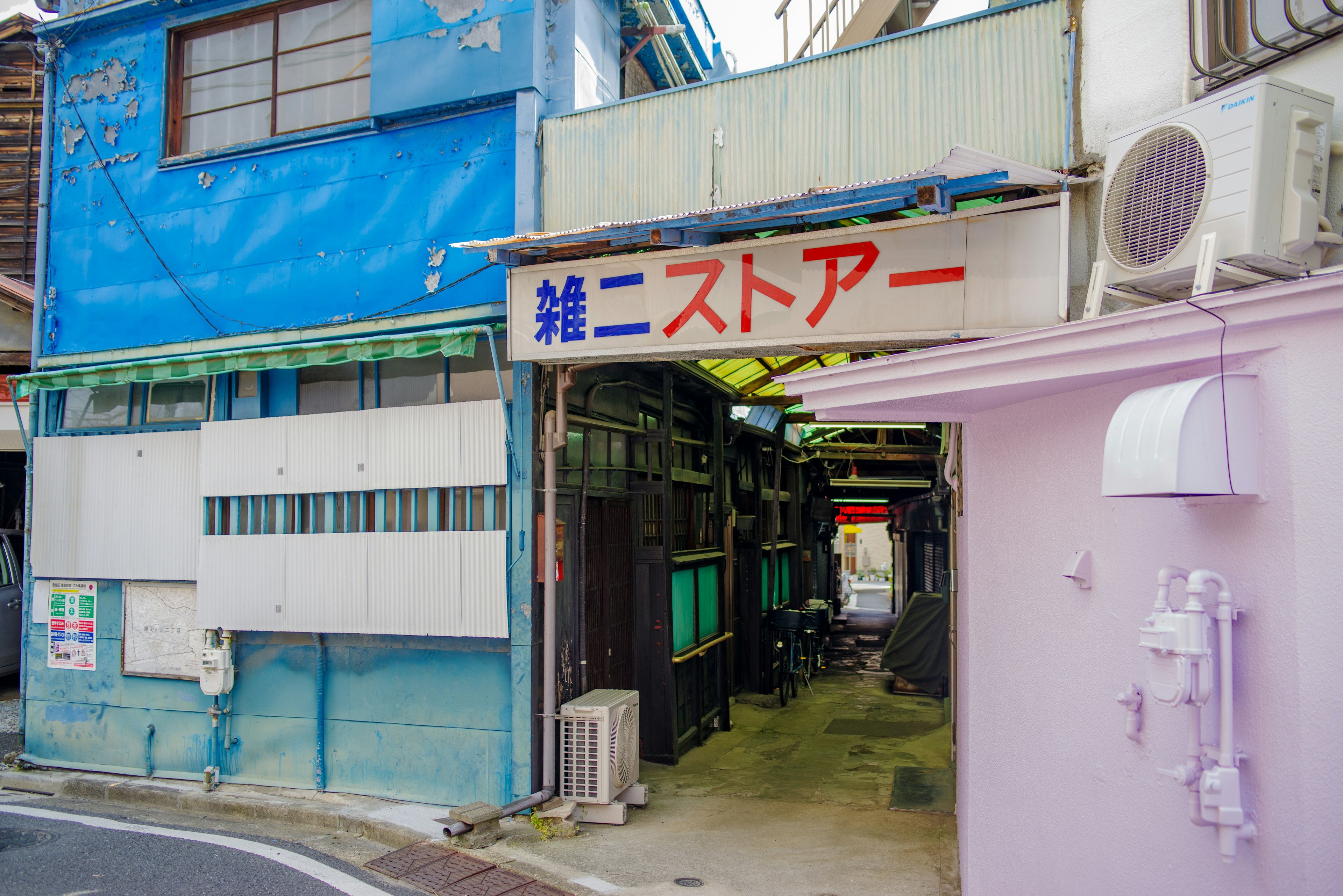 Entrada de un callejón estrecho con paredes azules y rosas que presenta un letrero en japonés