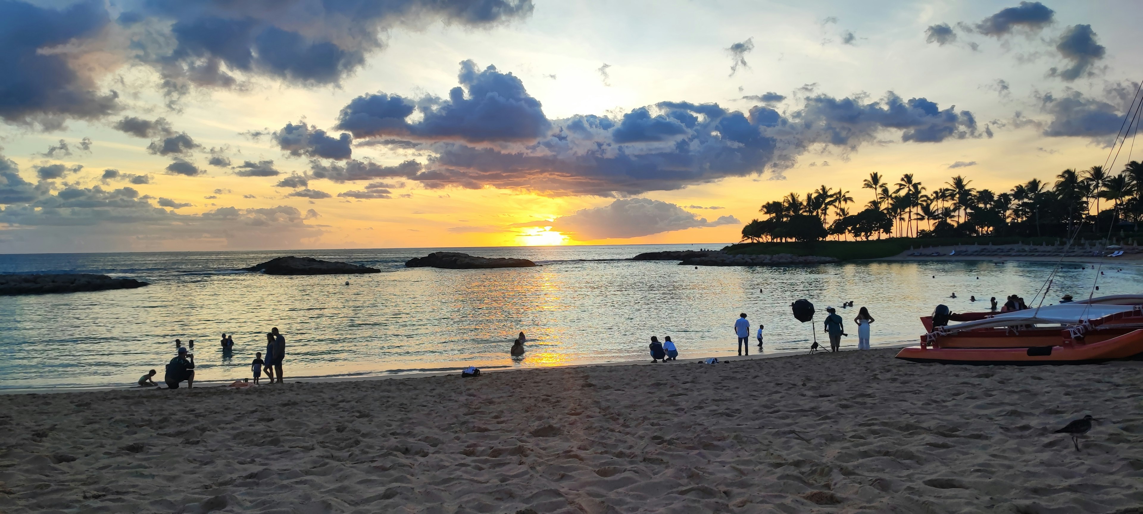 ทิวทัศน์ชายหาดที่สวยงามในขณะที่พระอาทิตย์ตก มีผู้คนเพลิดเพลินที่ชายฝั่ง