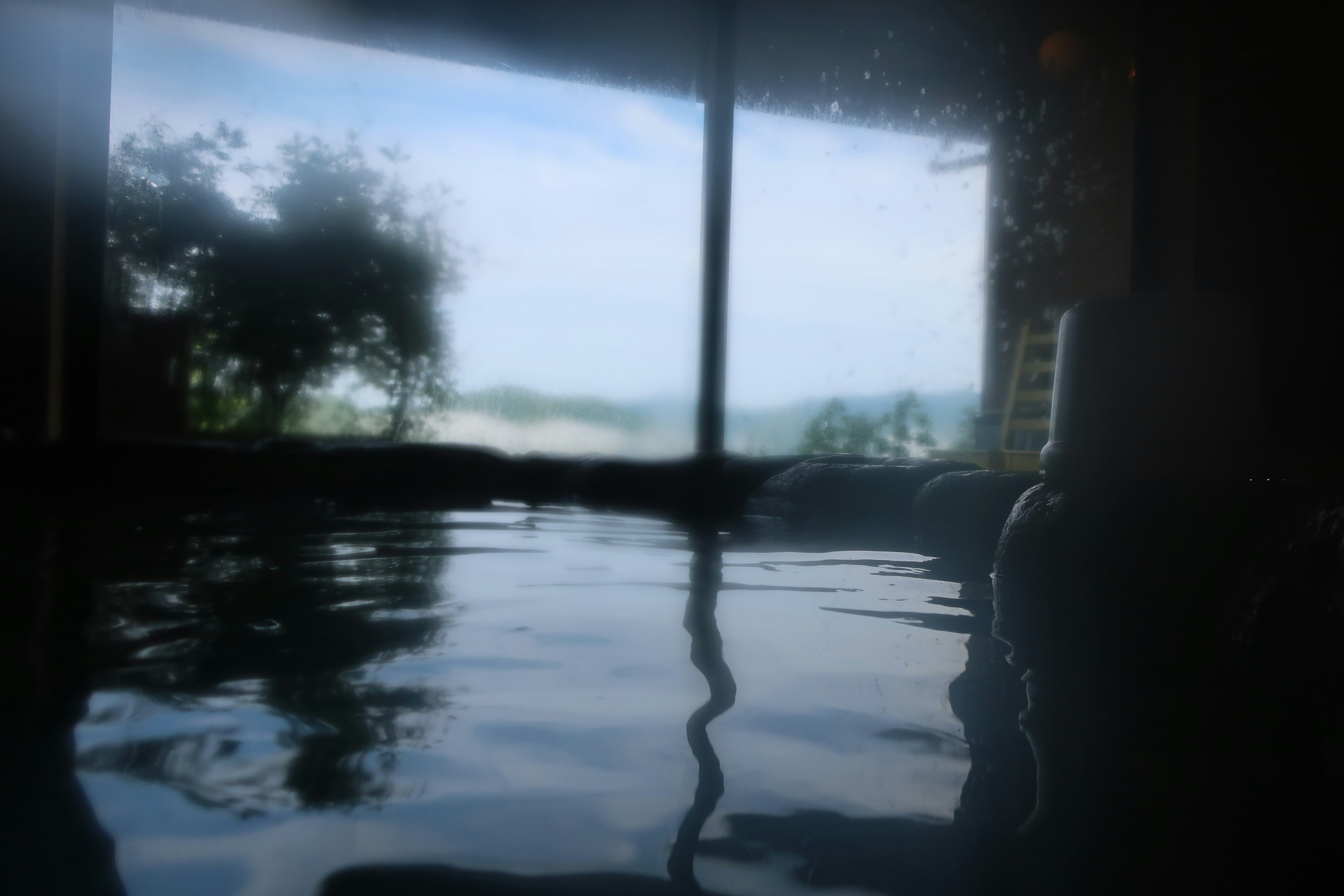 Serene hot spring water surface reflecting greenery outside the window