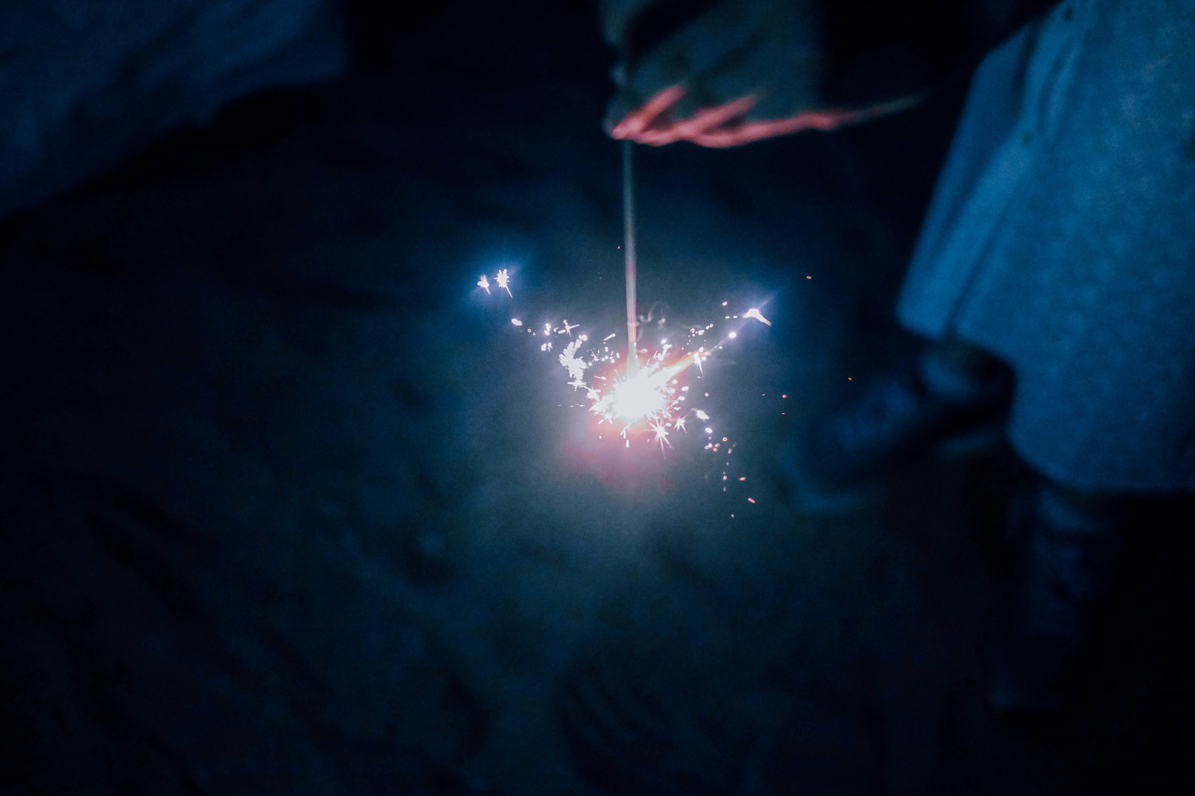 Mano che tiene un fuoco d'artificio che emette scintille luminose di notte