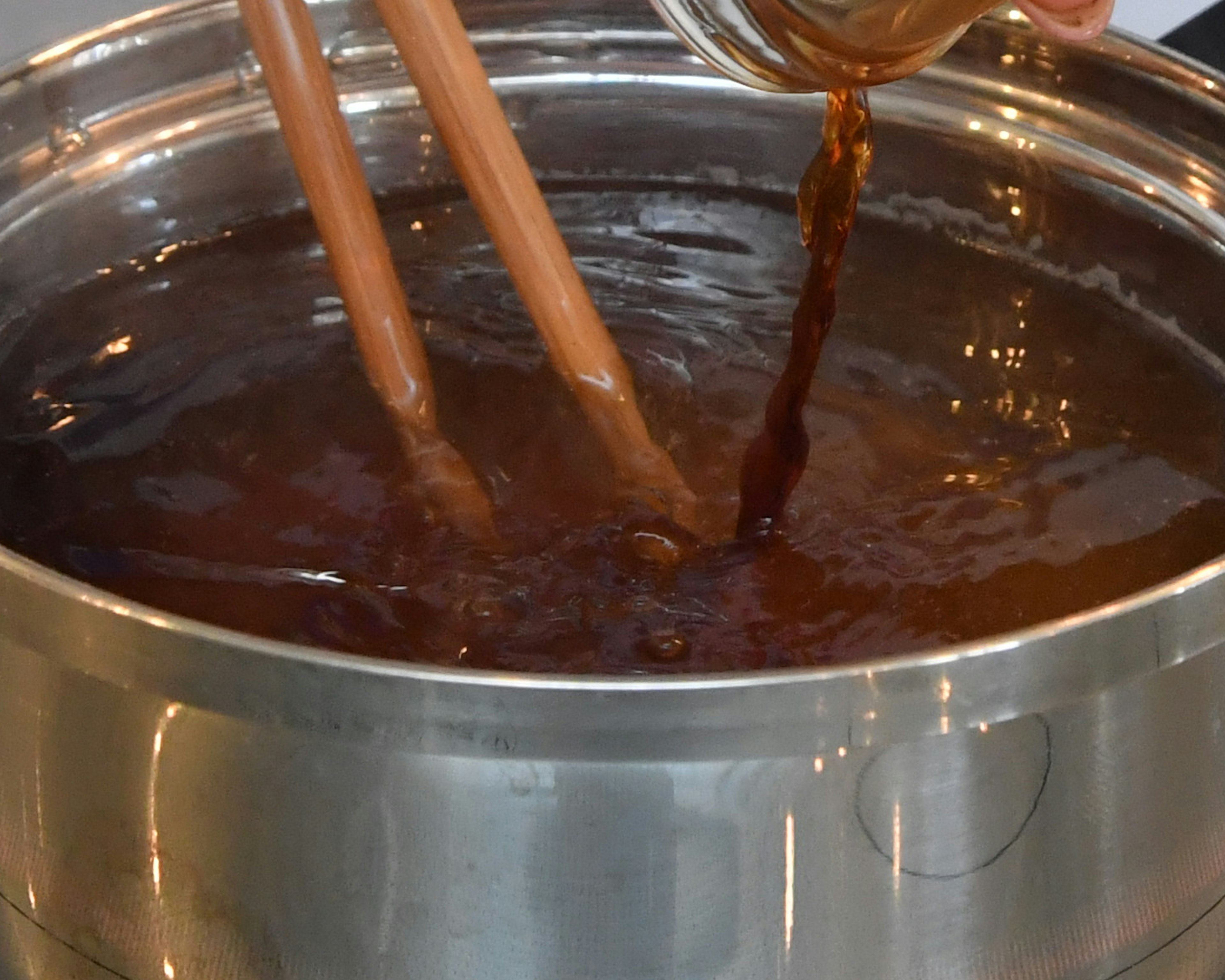 Vertiendo un líquido oscuro en una olla con palillos de madera