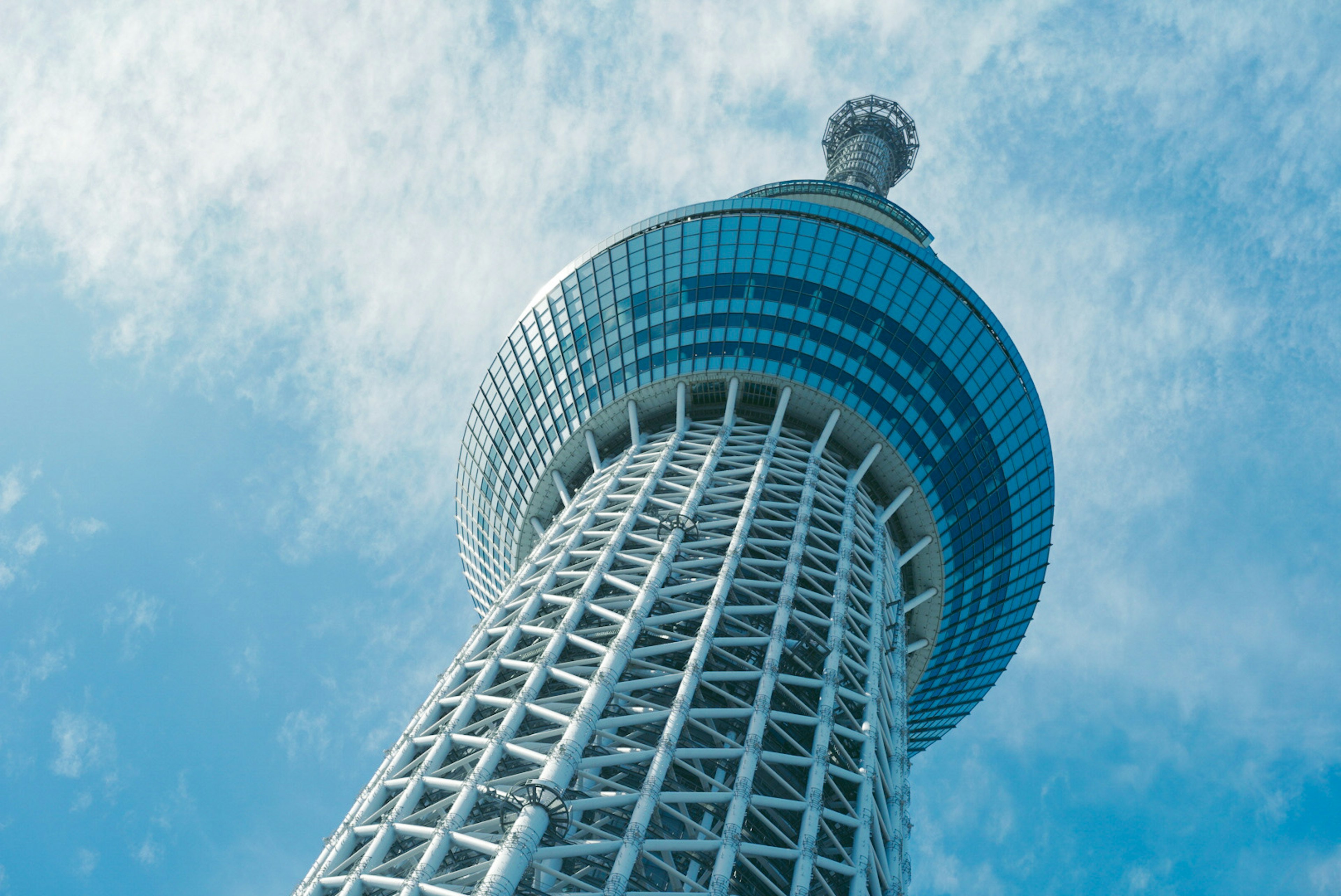 Pemandangan Tokyo Skytree dari bawah dengan langit biru dan awan di latar belakang menampilkan arsitektur modern