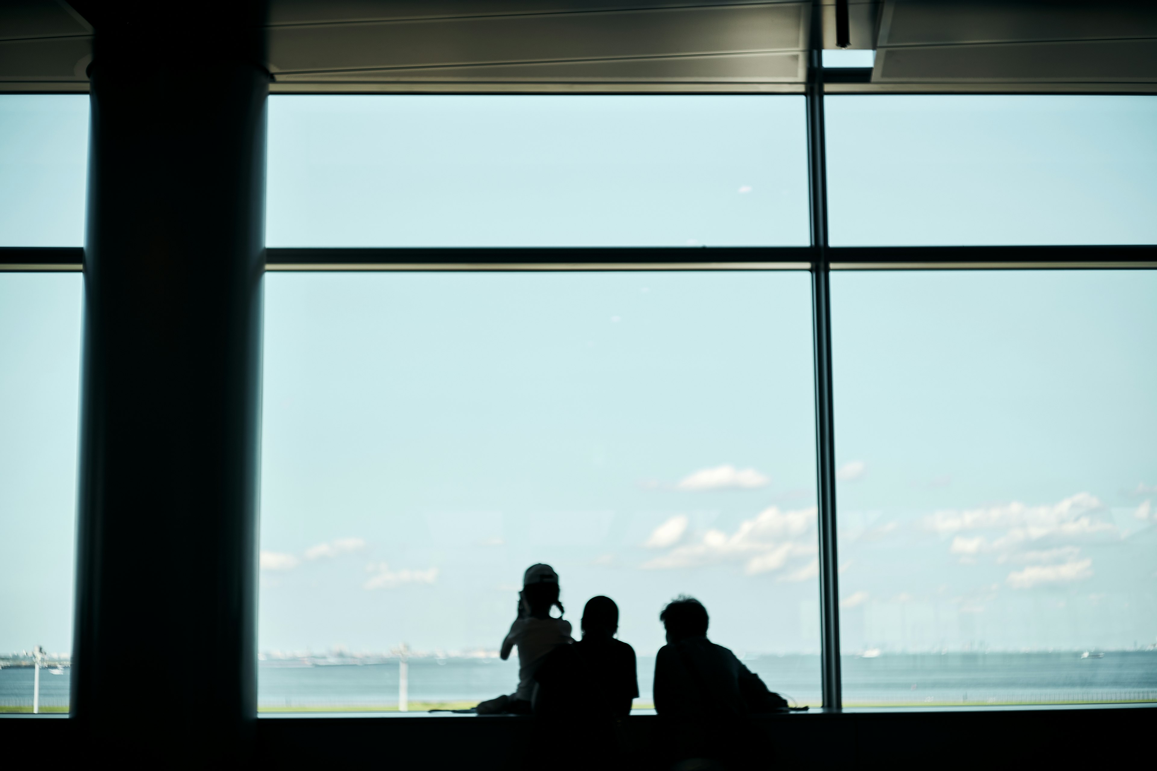 Silhouette einer Familie, die vor einem großen Flughafensfenster sitzt