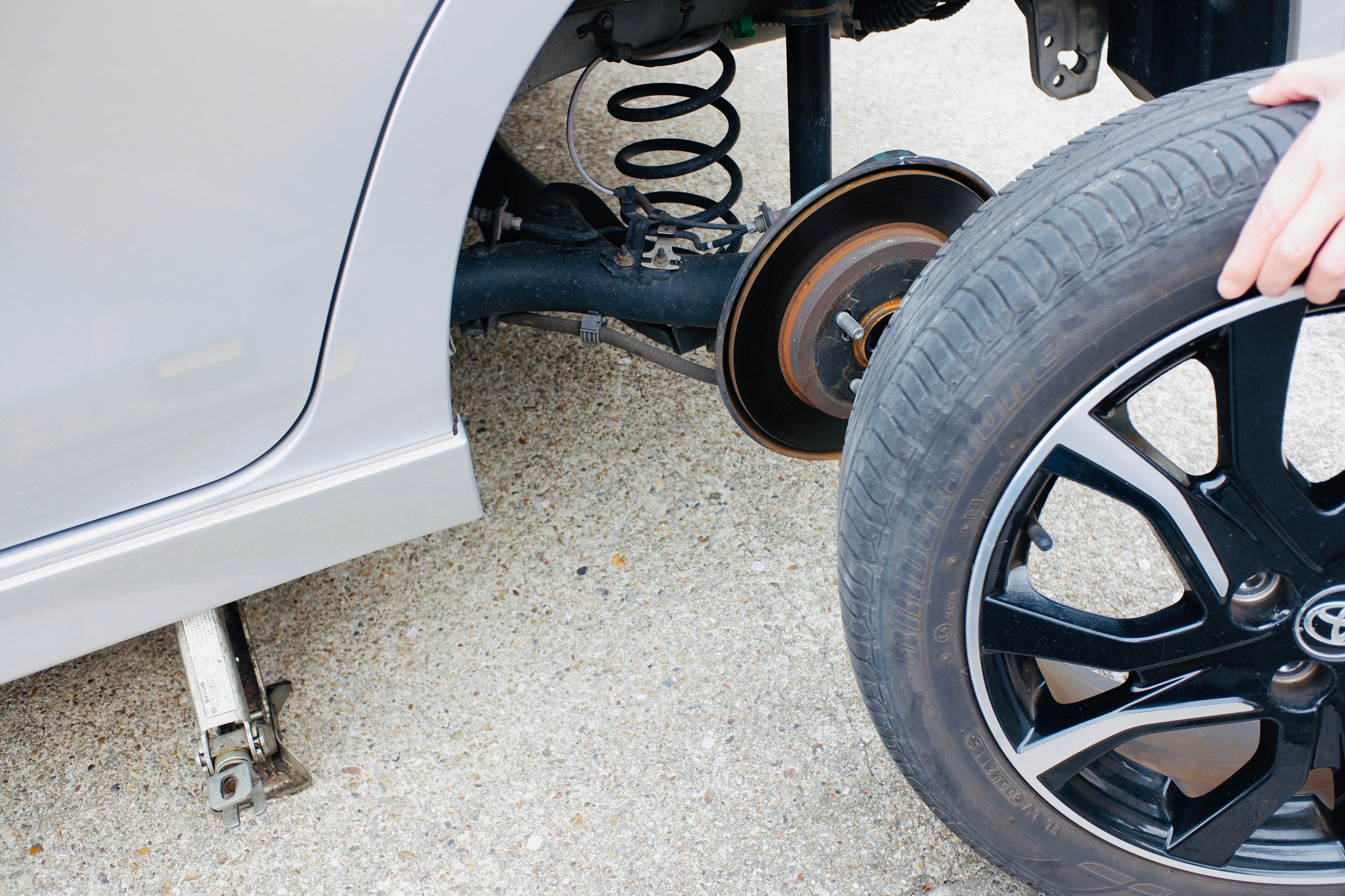 Part of a car lifted by a jack for tire replacement with a new tire being held