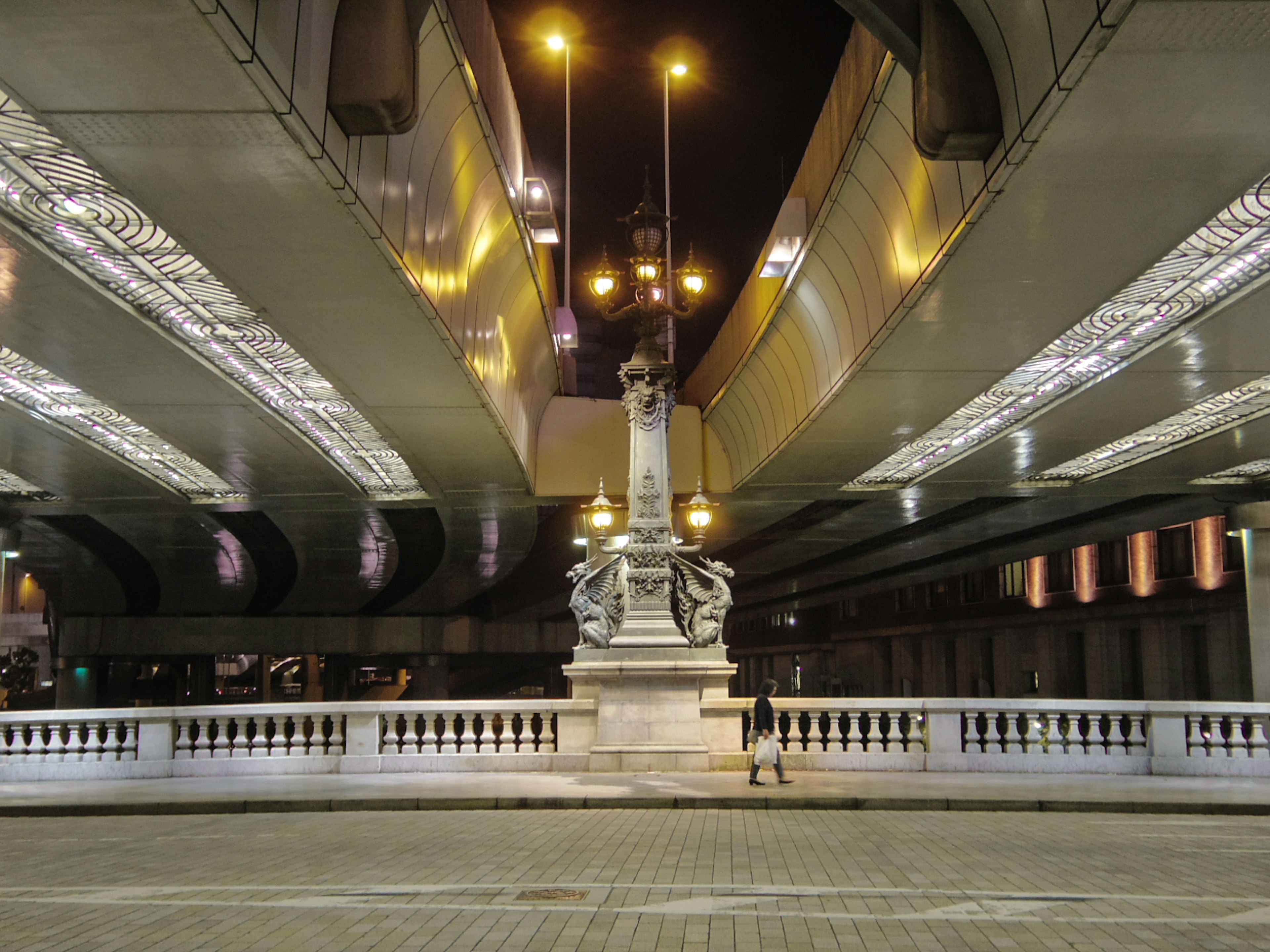 Nachtansicht einer Skulptur unter einer Brücke mit leuchtenden Straßenlaternen