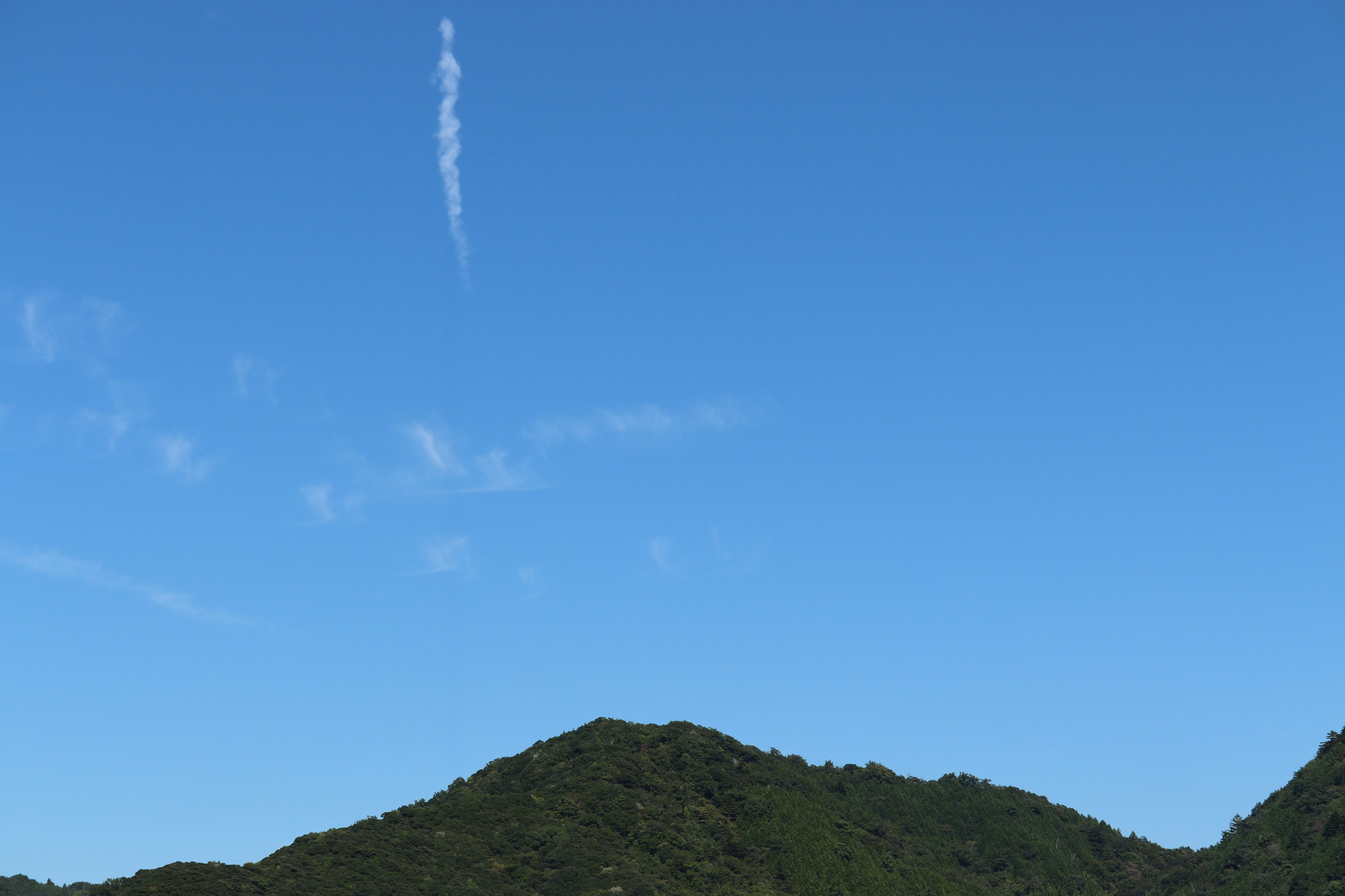 Mountain landscape under a clear blue sky with a contrail