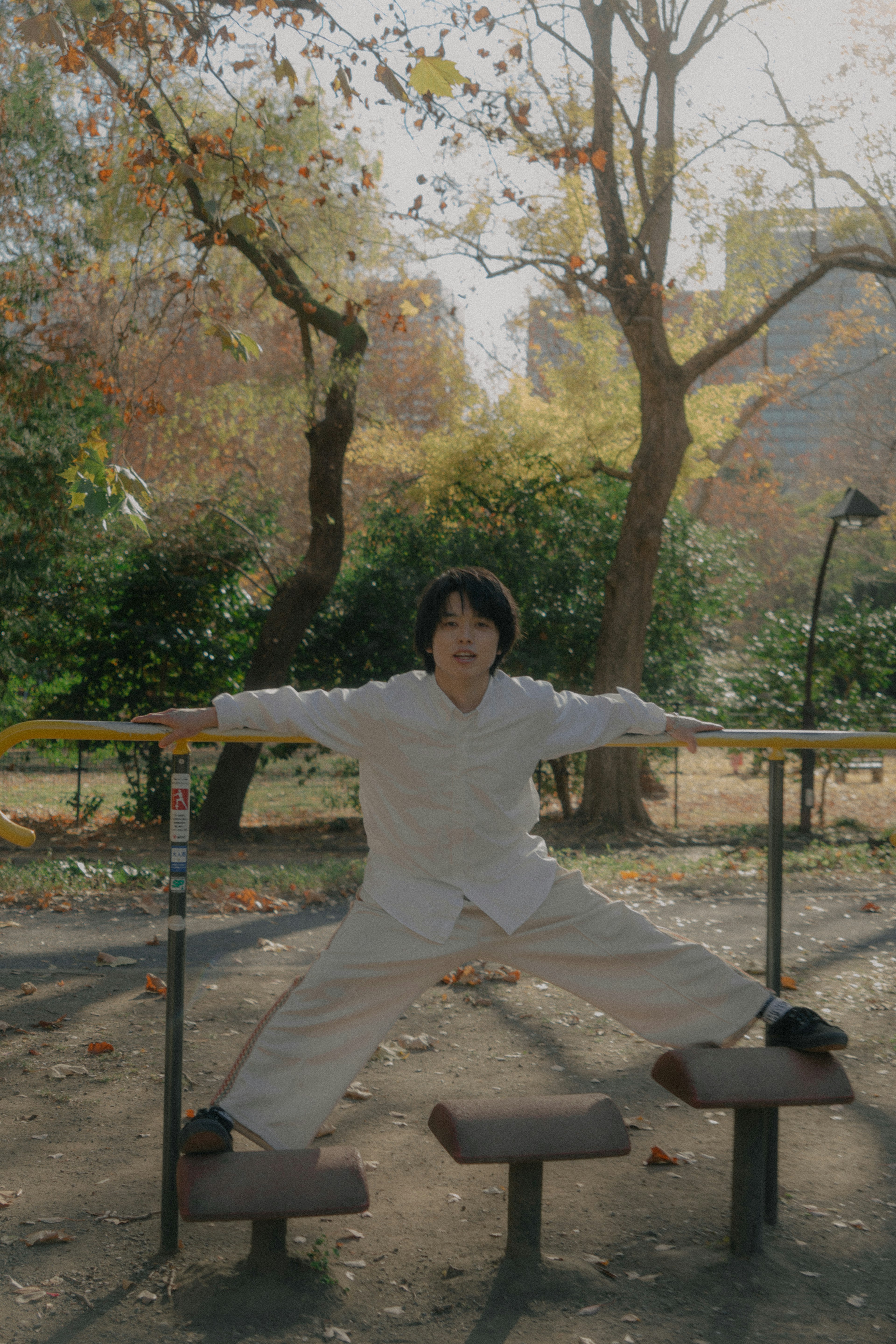 公園のバーにぶら下がる若い男性　自然の中でリラックスしたポーズ　周囲の木々と秋の色合い